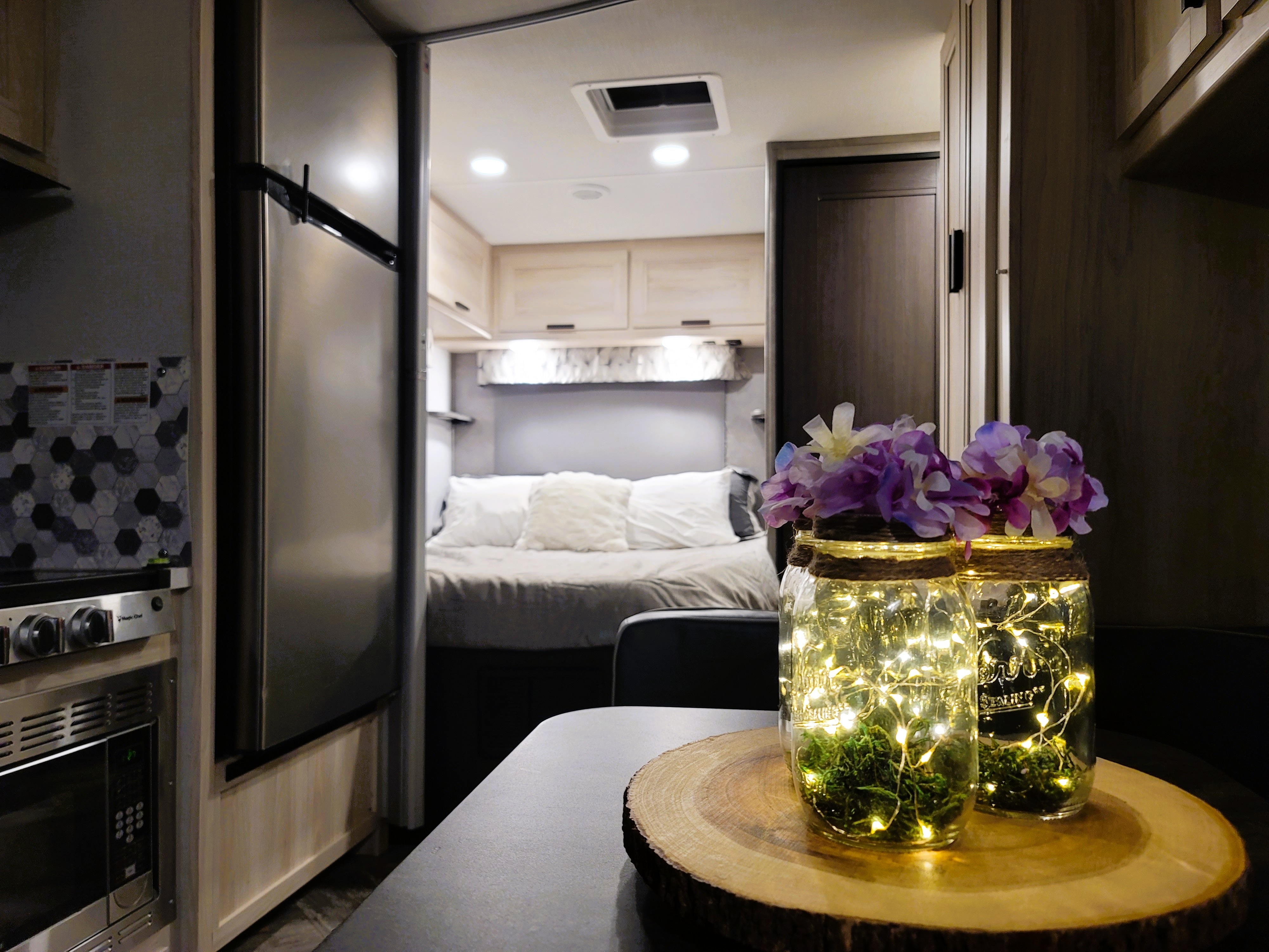 Inside a cozy RV rental: a modern kitchen on the left, a bedroom straight ahead, and decorative glowing jars on the table.. Forest River Sunseeker LE 2022
