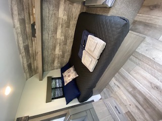 Cozy RV rental interior with a comfortable dark bed/sofa, rustic wood-paneled walls, and light flooring for travel.. Keystone Springdale 2021