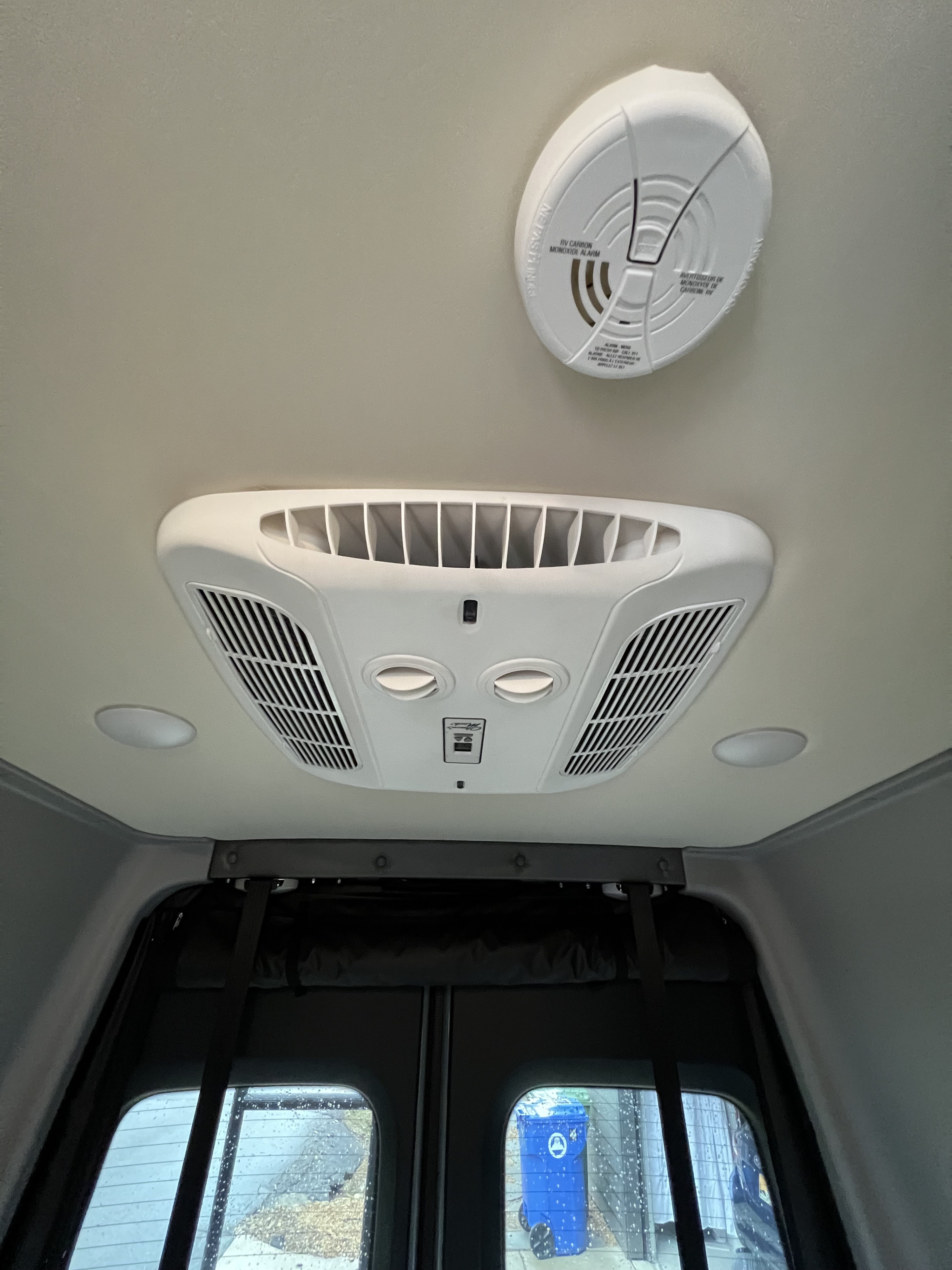 RV rental ceiling: AC unit, carbon monoxide alarm, recessed lights, and window view outside a vehicle.. Winnebago Revel 2023