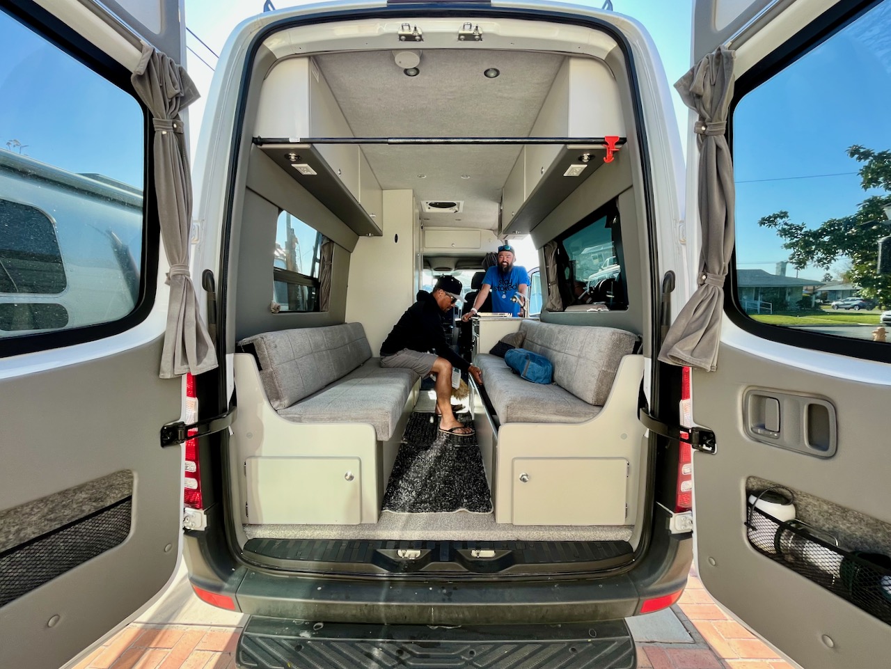 Rear view of an **RV rental**: a custom camper van interior with two men, comfortable bench seating, and ample storage for trips.. Sportsmobile Regular Body 2017