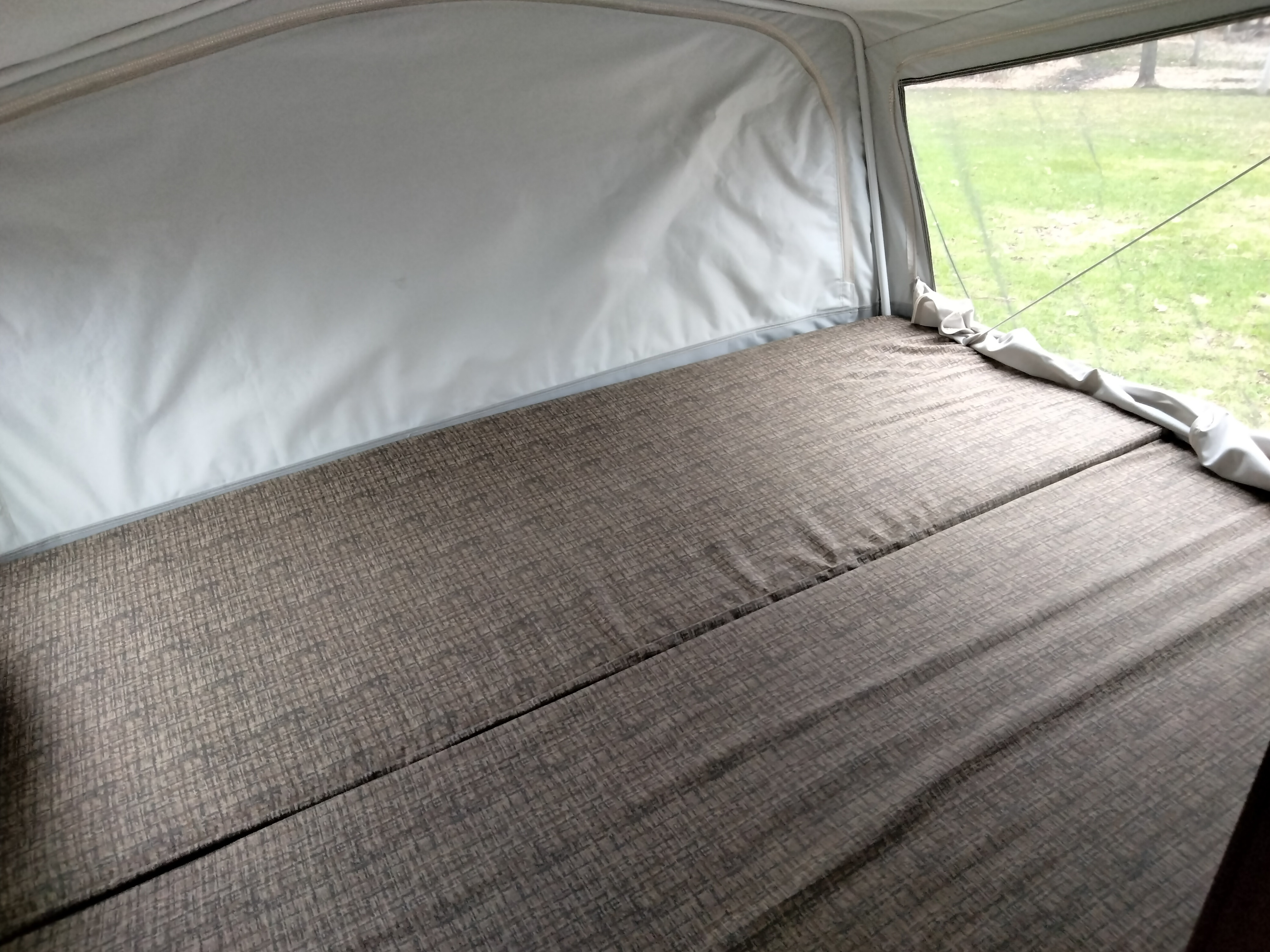 Inside an **rv rental** pop-up camper: a textured bed mattress and side canvas wall, with a clear window view of green outdoors.. Jayco Jay Feather Ultra Lite 2013