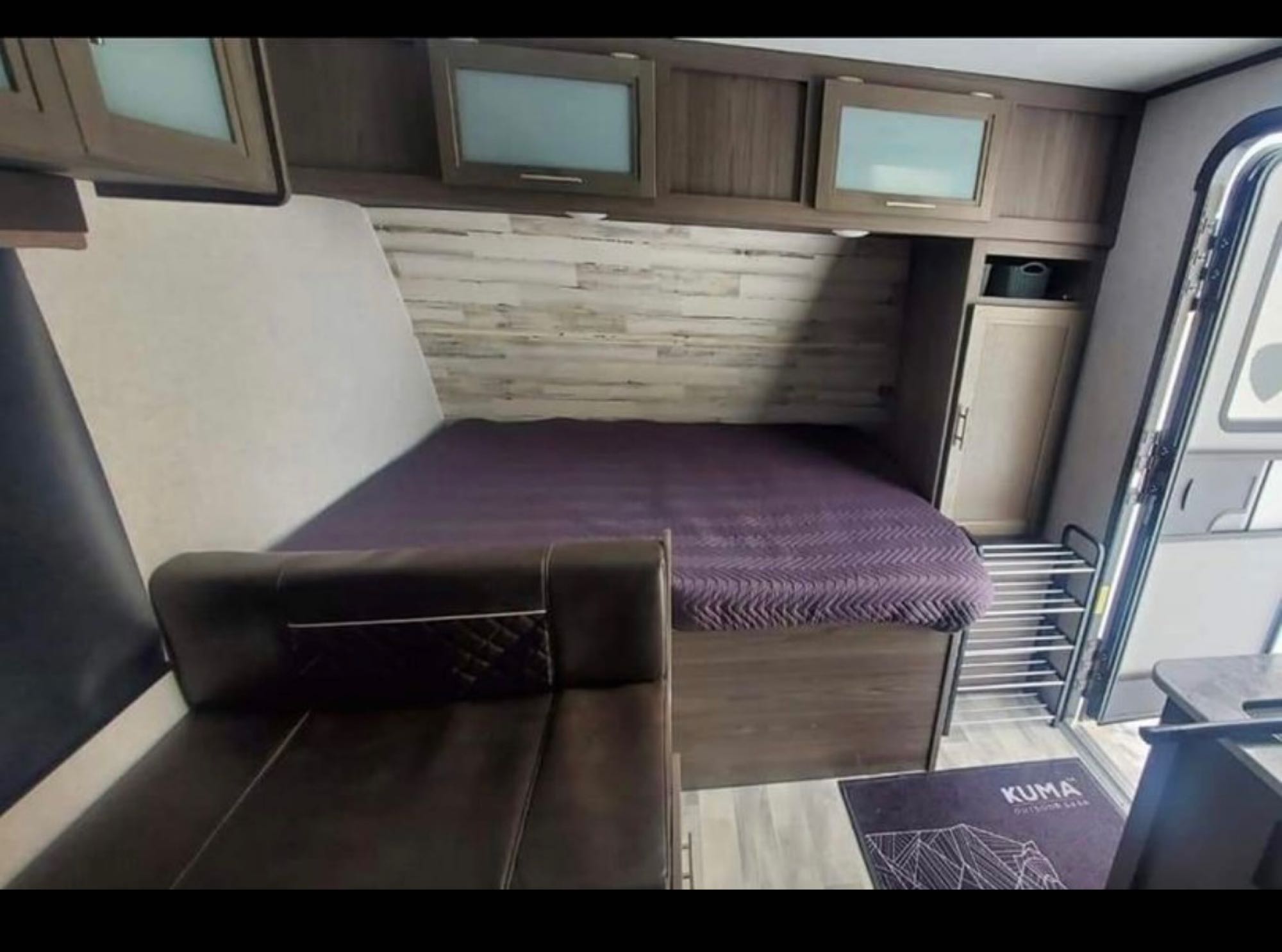 RV rental interior view: a cozy bed with purple cover, leather seating, and overhead cabinets offer comfort.. Dutchmen Kodiak 2021