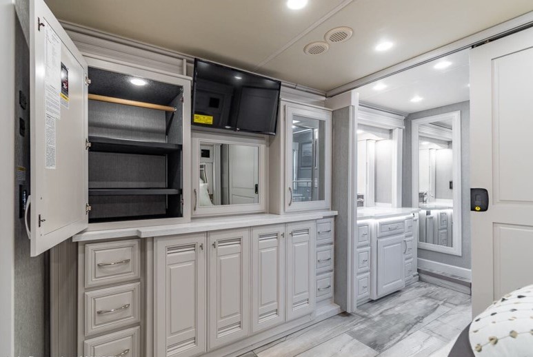 Modern RV rental bedroom-bathroom area. Features include extensive light-colored cabinetry, TV, and spacious vanity. Ready for your adventure.. Holiday Rambler Armada 2023