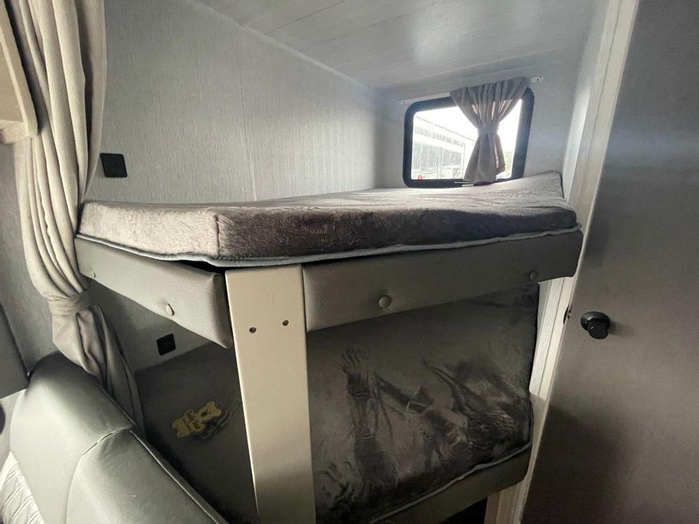Inside an RV rental: two comfy bunk beds with soft mattresses, a window, and a privacy curtain. Ideal for family travel.. Forest River Wildwood Xlite 2023