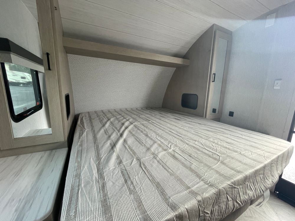 Explore this cozy rv rental bedroom: a comfortable bed with striped linens, built-in storage, and a window view.. Forest River Wildwood Xlite 2023