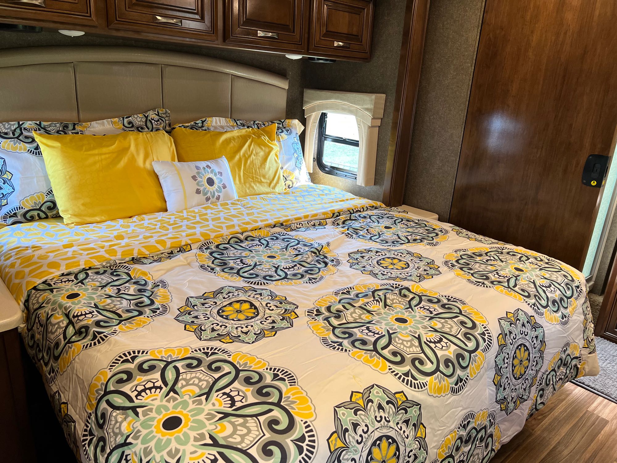 Cozy RV rental bedroom features vibrant yellow and patterned bedding, built-in wooden cabinets, and a small window.. Thor Miramar 2018