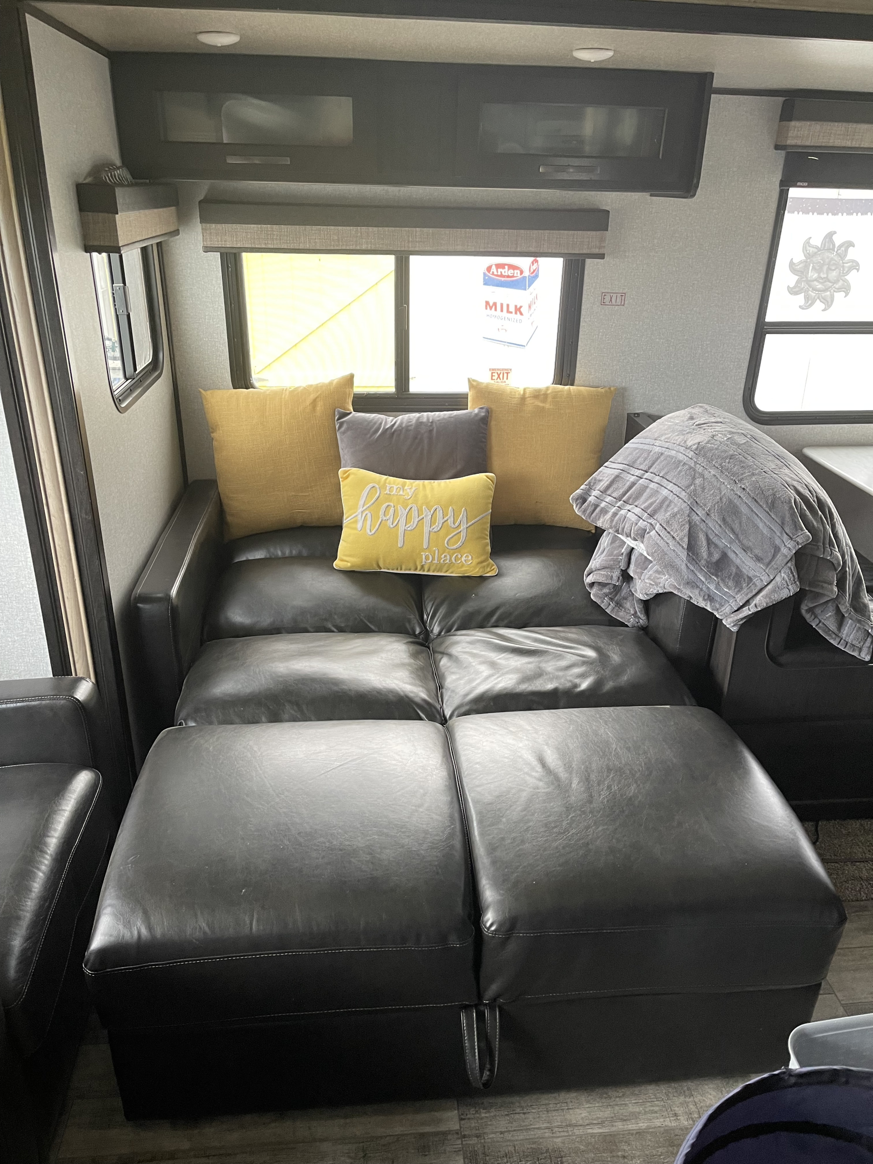 RV rental cozy interior featuring a black leather sofa bed with yellow and gray pillows, and a soft blanket.. Forest River Surveyor Luxury 2020