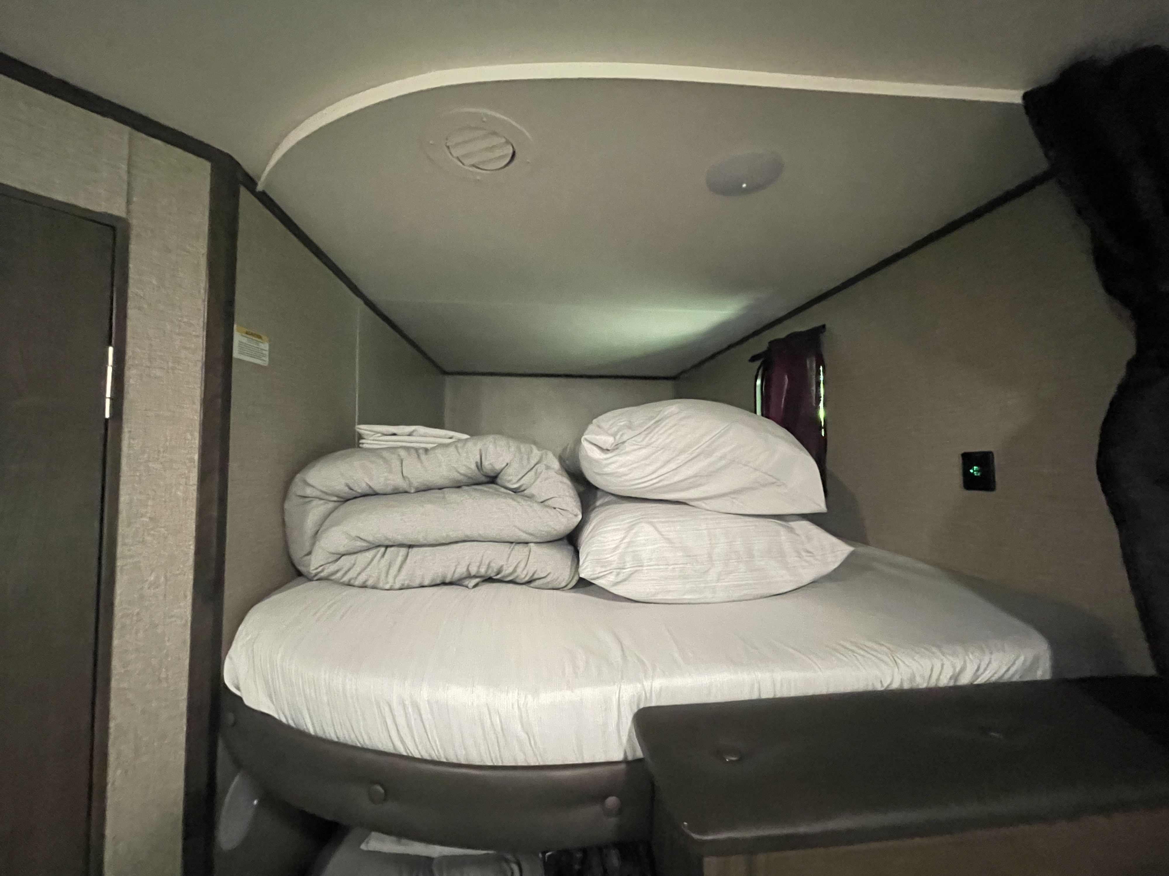 Inside an RV rental: a compact bedroom with neatly arranged bed, pillows, and folded comforter, set for comfortable travel.. Jayco Jay Flight SLX 2021
