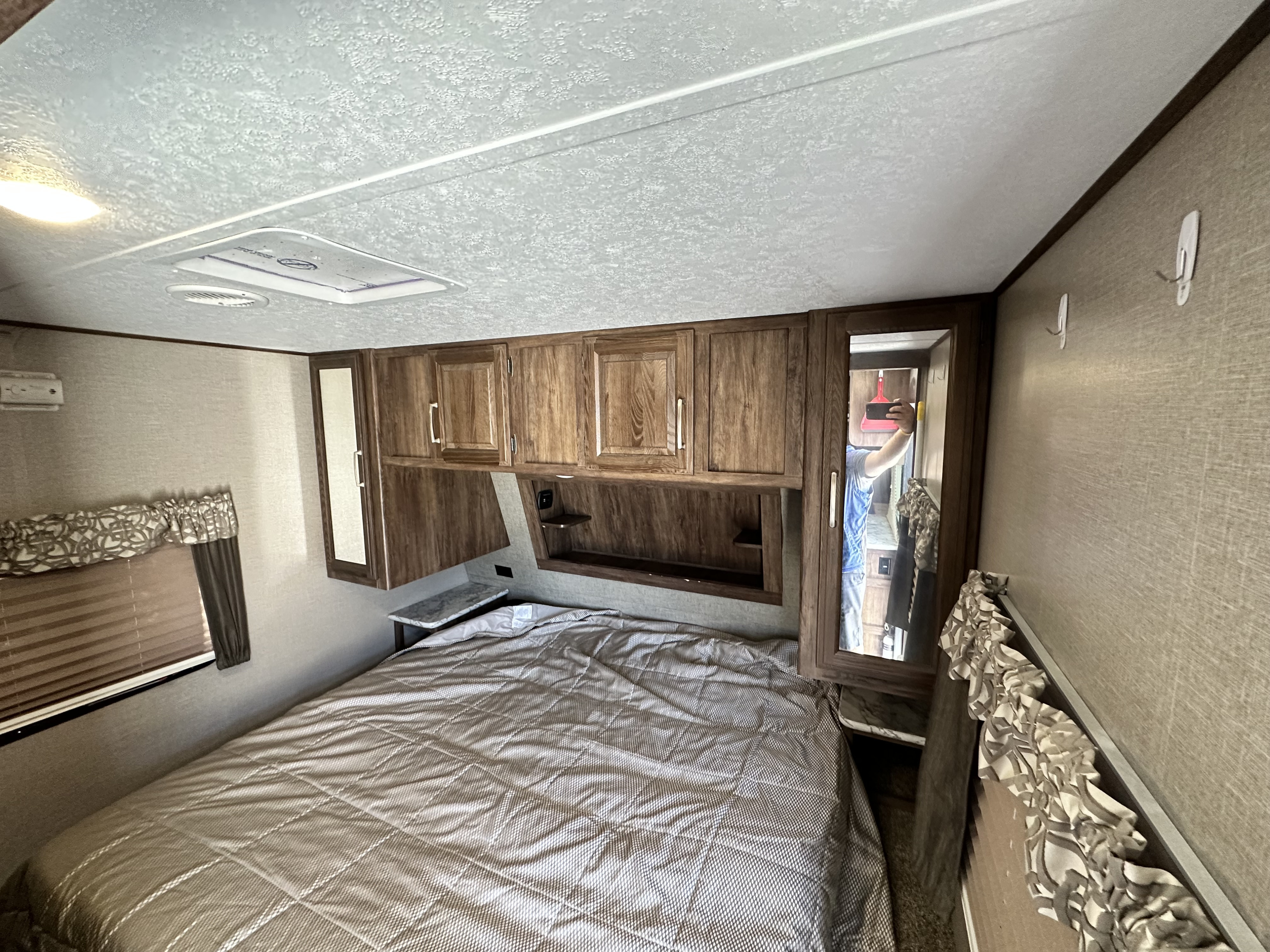 RV rental bedroom features a patterned bed, wooden overhead cabinets, mirrored closet, and window. Great for travel!. Keystone RV Cougar 2018