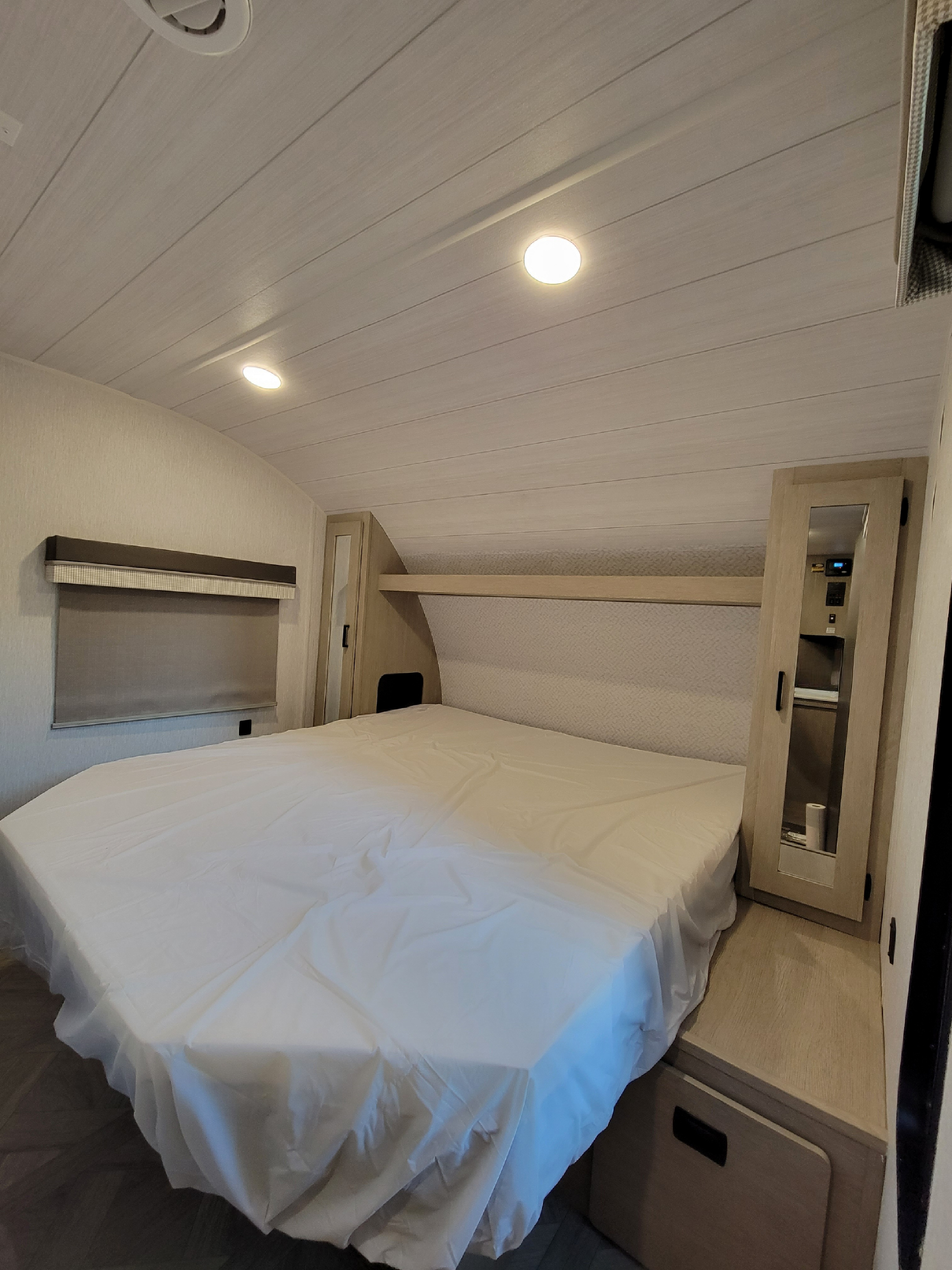 Step into this cozy RV rental bedroom. It features a spacious bed with a clean white cover, built-in storage, and a privacy window shade.. Forest River 31bhxl 2023
