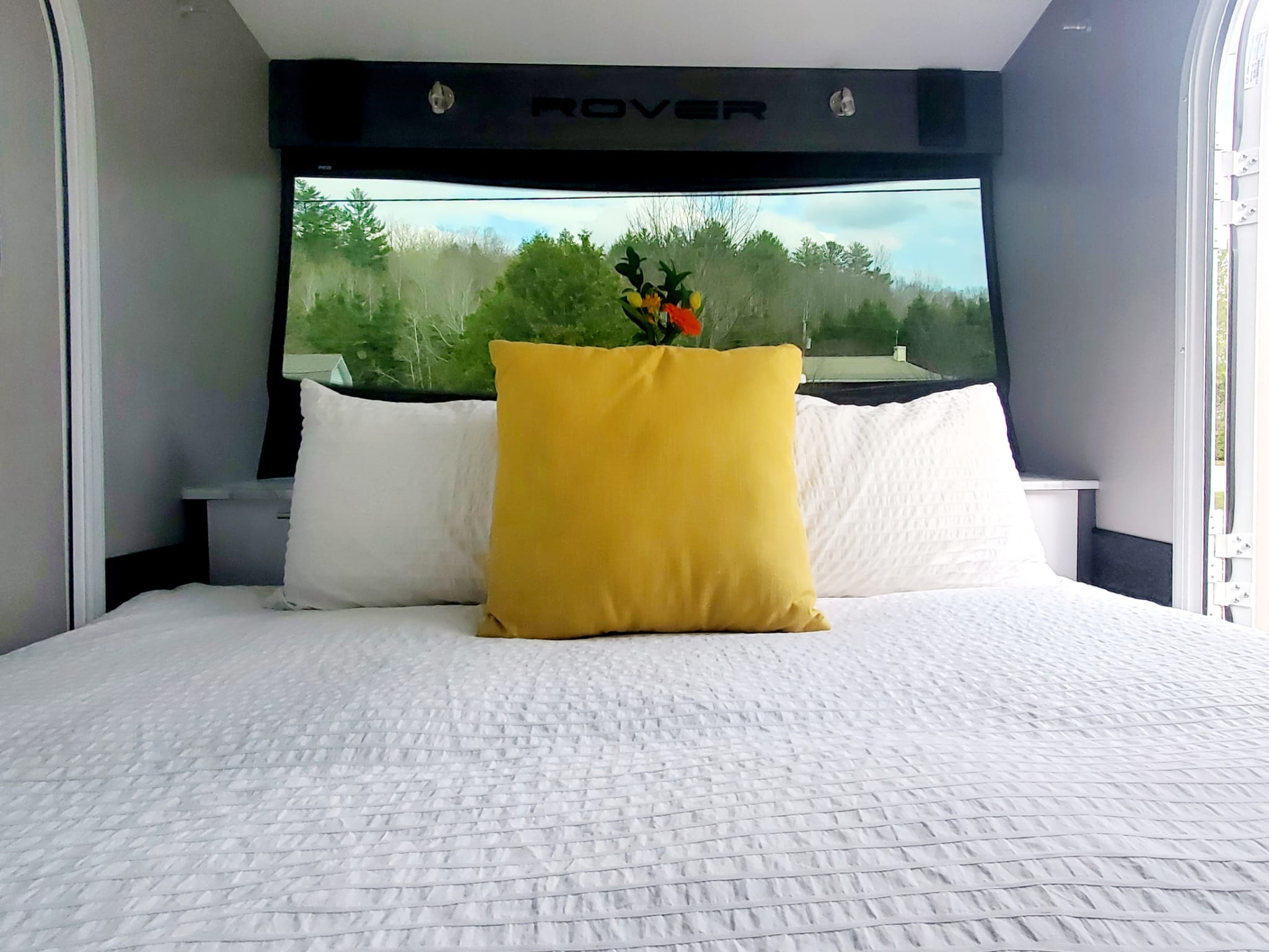 Experience an RV rental! This comfy Rover RV bedroom features a large bed, yellow accent pillow, and panoramic forest views.. Intech Luna Rover 2023