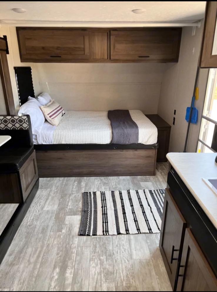 Inside an RV rental: a compact sleeping area with bed, storage, and dinette. Light wood-look floor, striped rug.. Avenger Avenger Trailer 2021