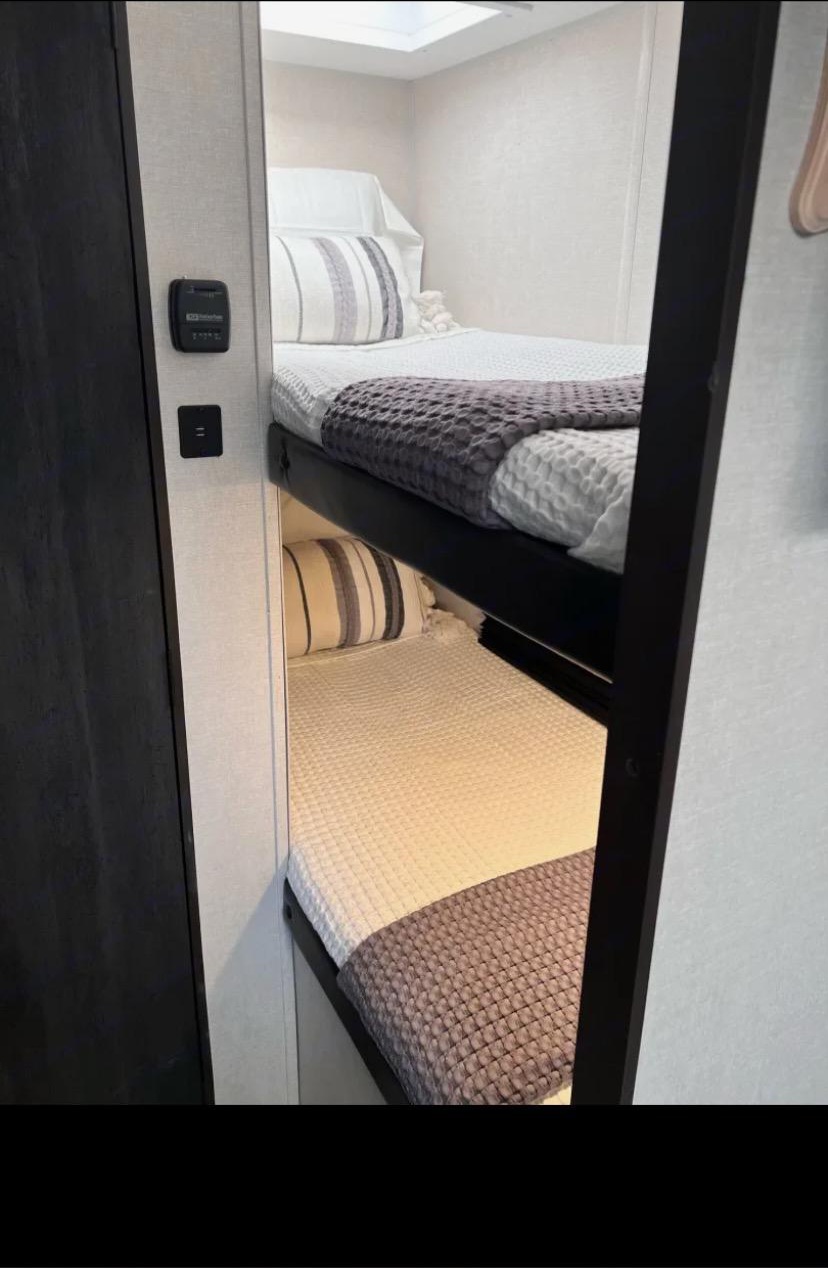 Cozy RV rental bunk beds with clean white bedding and striped pillows, perfect for a compact, comfortable sleeping area.. Avenger Avenger Trailer 2021