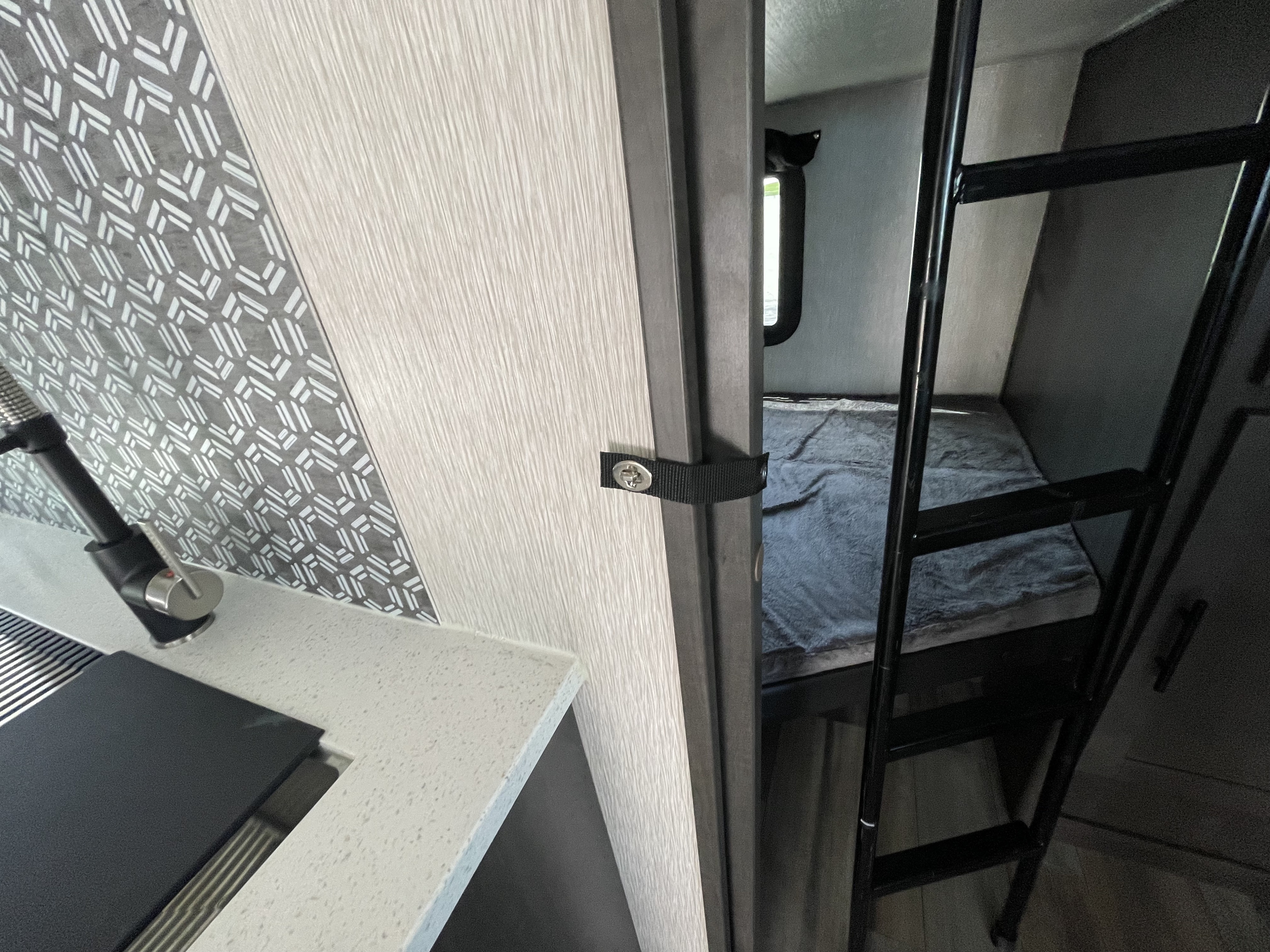 View inside an RV rental: modern kitchen counter with faucet, patterned wall, and a cozy bunk bed area with a ladder.. Crossroads Cruiser Aire 2023