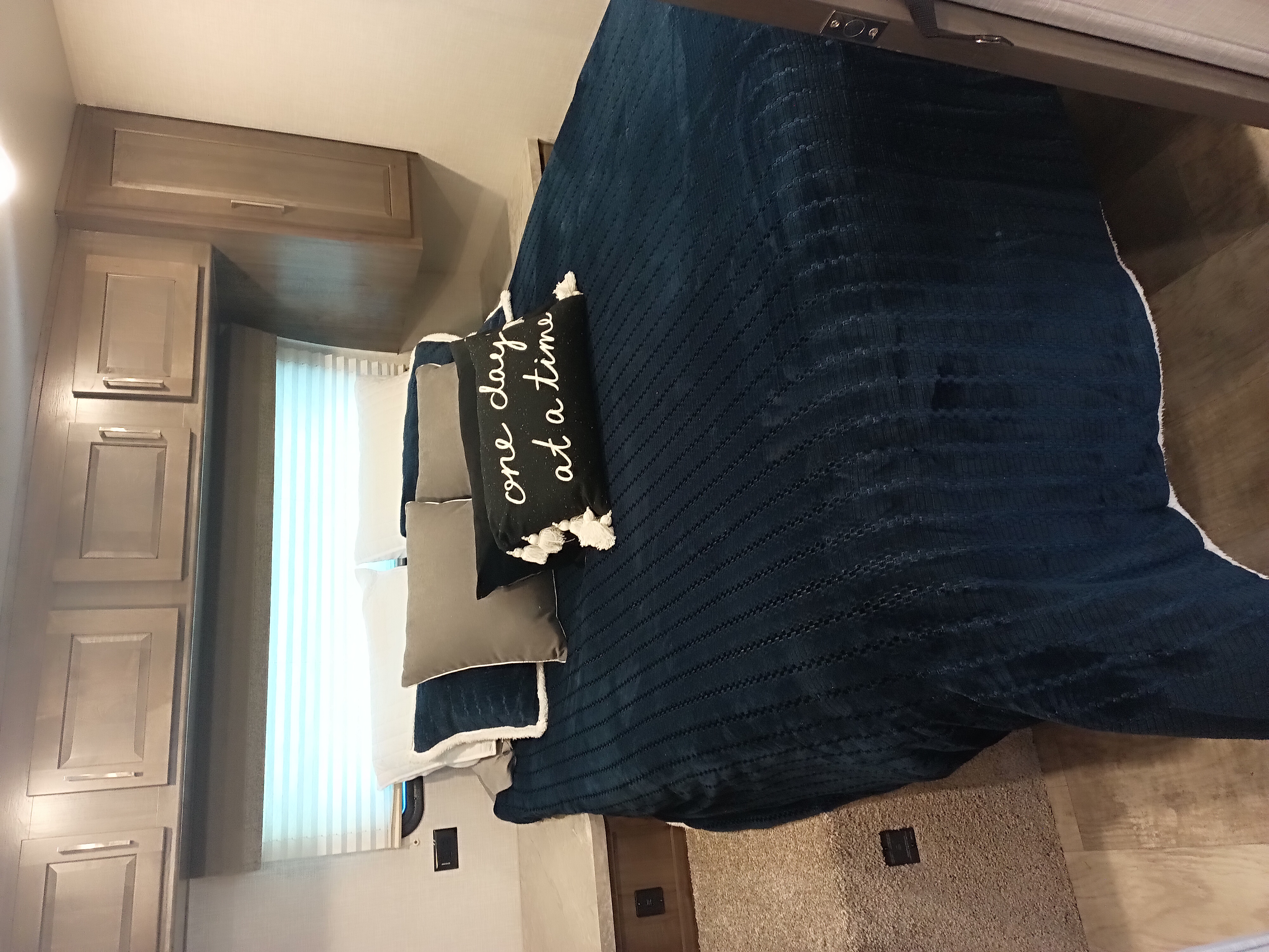 RV rental bedroom featuring a bed with a blue comforter, decorative pillows, and overhead storage cabinets.. Forest River Flagstaff Micro Lite 2022