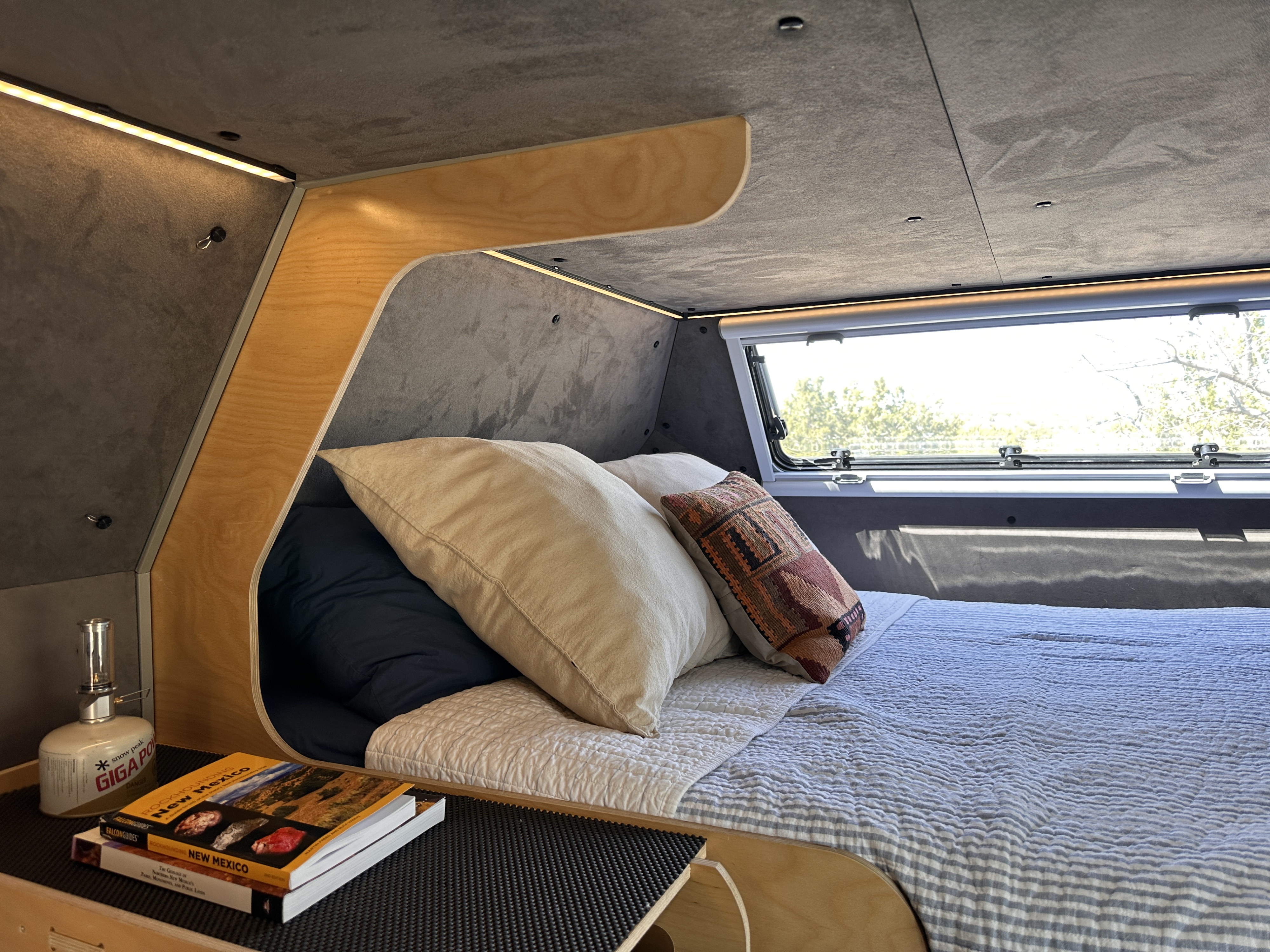 Cozy RV rental bedroom with ambient lighting, a comfortable bed, travel books, and a clear window view for your adventure.. Kimbo Kimbo 6 2020