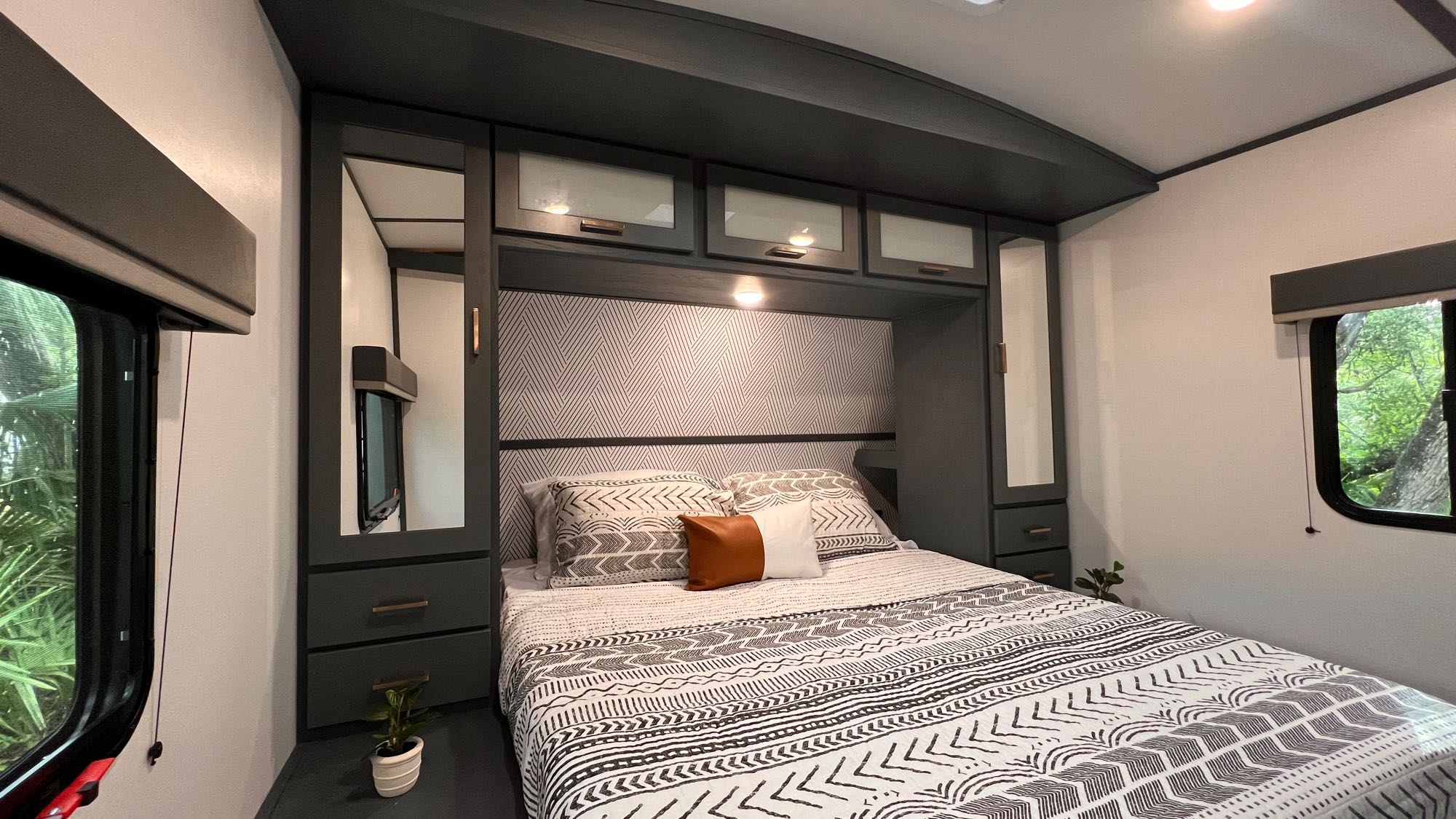 Modern RV rental bedroom featuring a queen bed with patterned bedding, built-in storage, and side windows.. Keystone RV Bullet Ultra Lite 2022