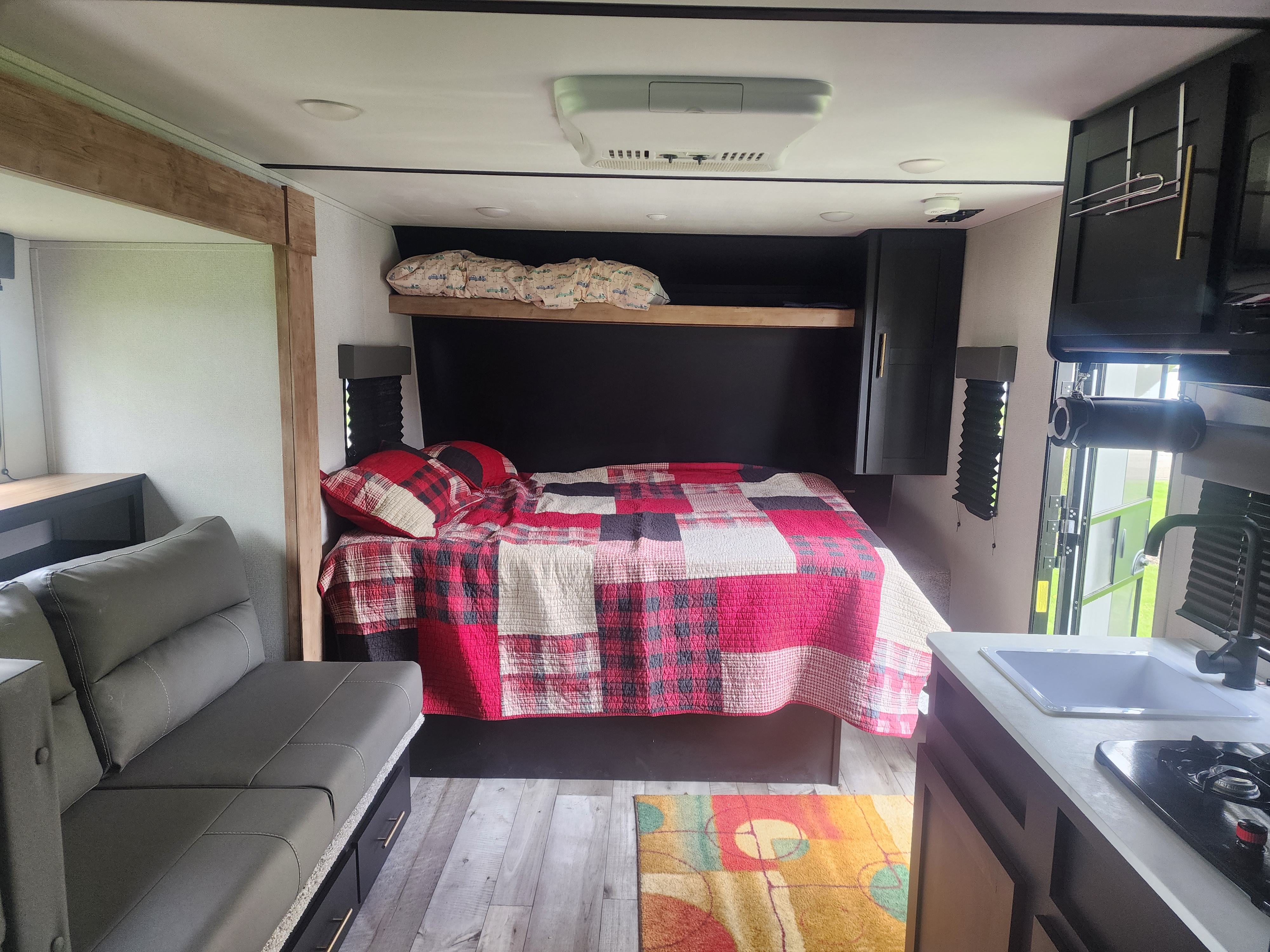 Cozy RV rental interior featuring a comfy bed, gray sofa, and compact kitchen area.. Keystone RV Springdale 2022