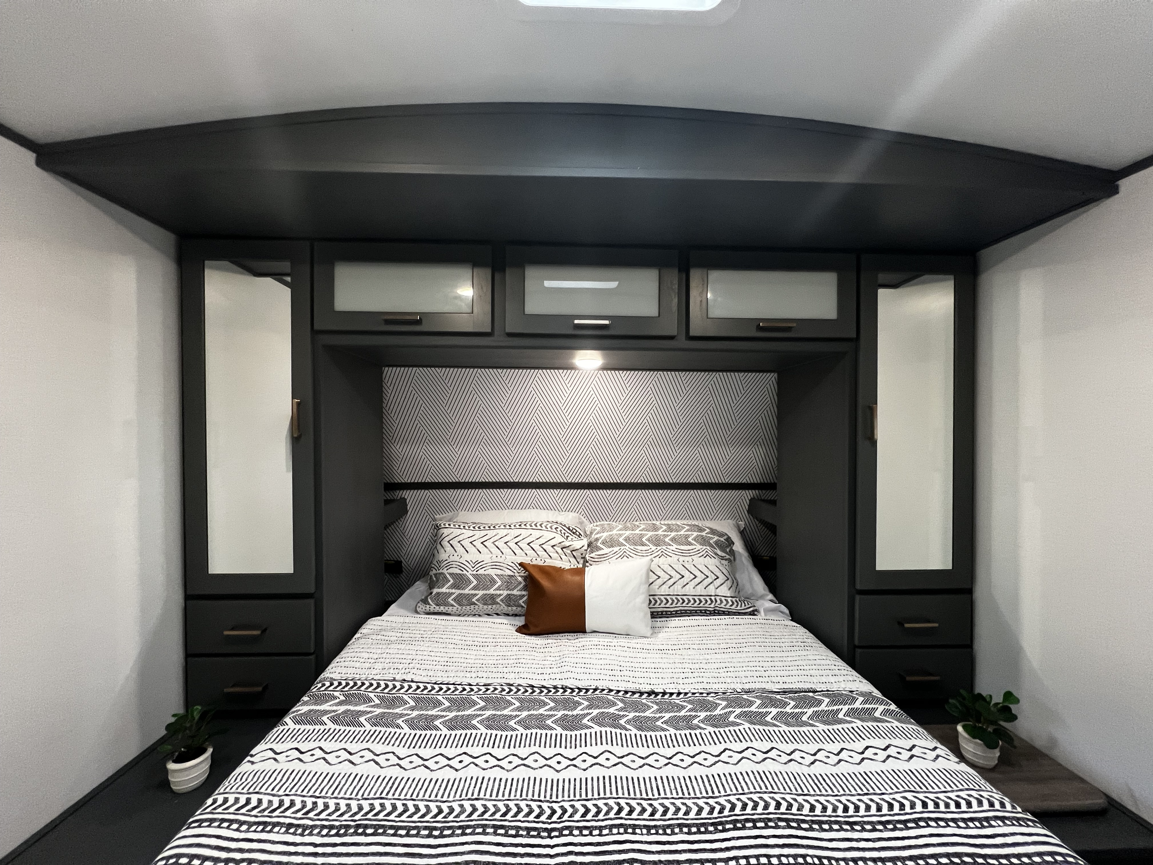 Modern RV rental bedroom with black and white patterned bedding, dark storage cabinets, and ambient lighting. Features bedside plants.. Keystone RV Bullet Ultra Lite 2022