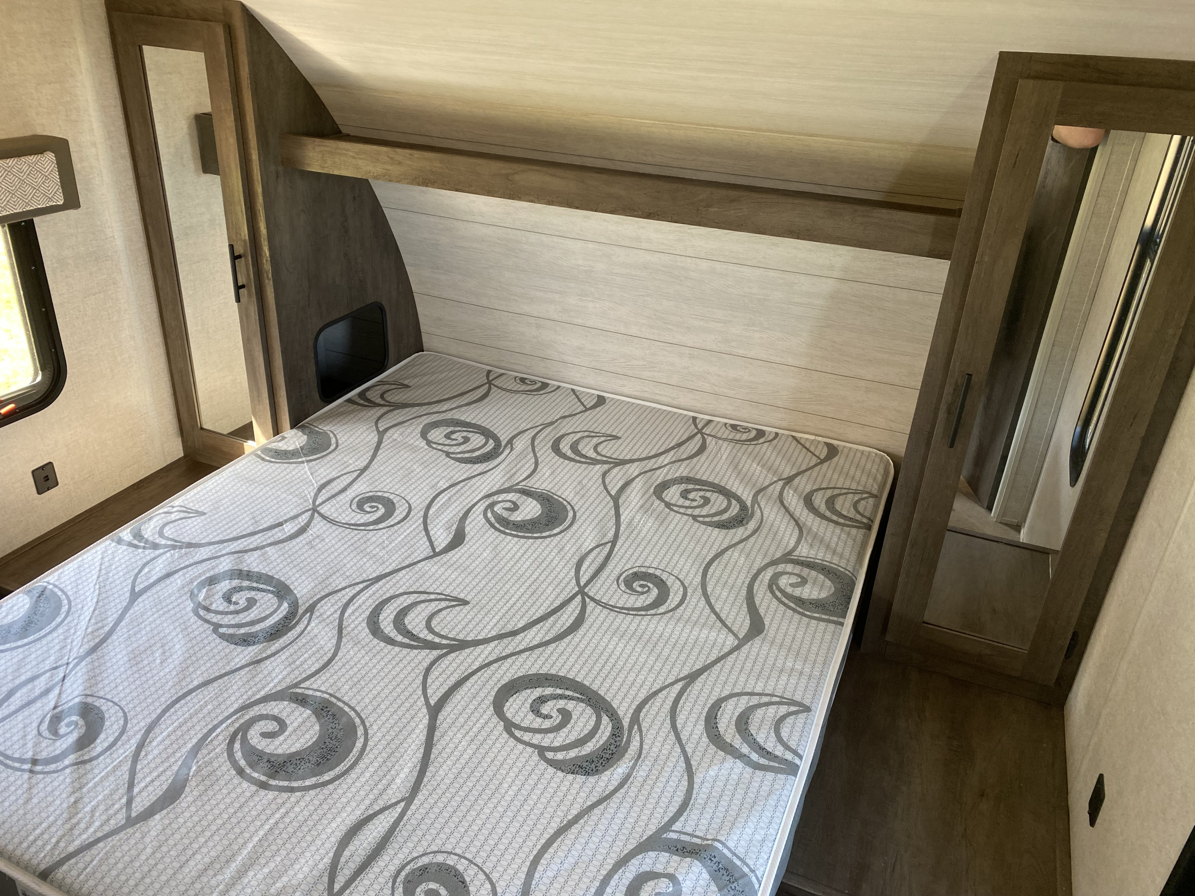 Compact RV rental bedroom with patterned mattress, mirrored wardrobes, and overhead storage. A functional travel space.. Forest River Salem Cruise Lite 2021