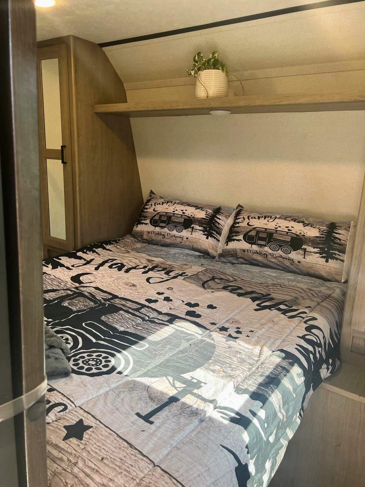 Cozy RV rental bedroom featuring a "Happy Camping" themed bed, built-in storage, and an overhead shelf.. Keystone RV Hideout Luxury 2021