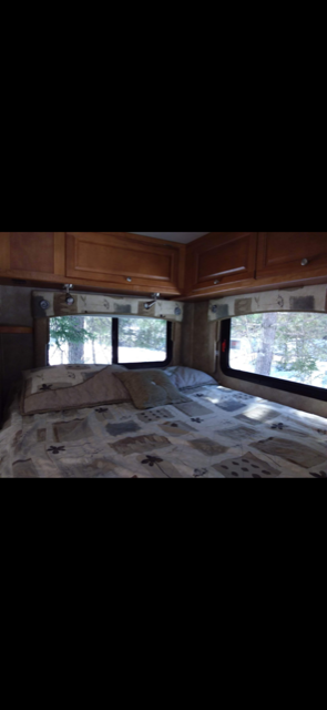 Cozy RV rental bedroom featuring a comfy bed, overhead cabinets, and large windows with outdoor views.. Gulf Stream Ultra 2009
