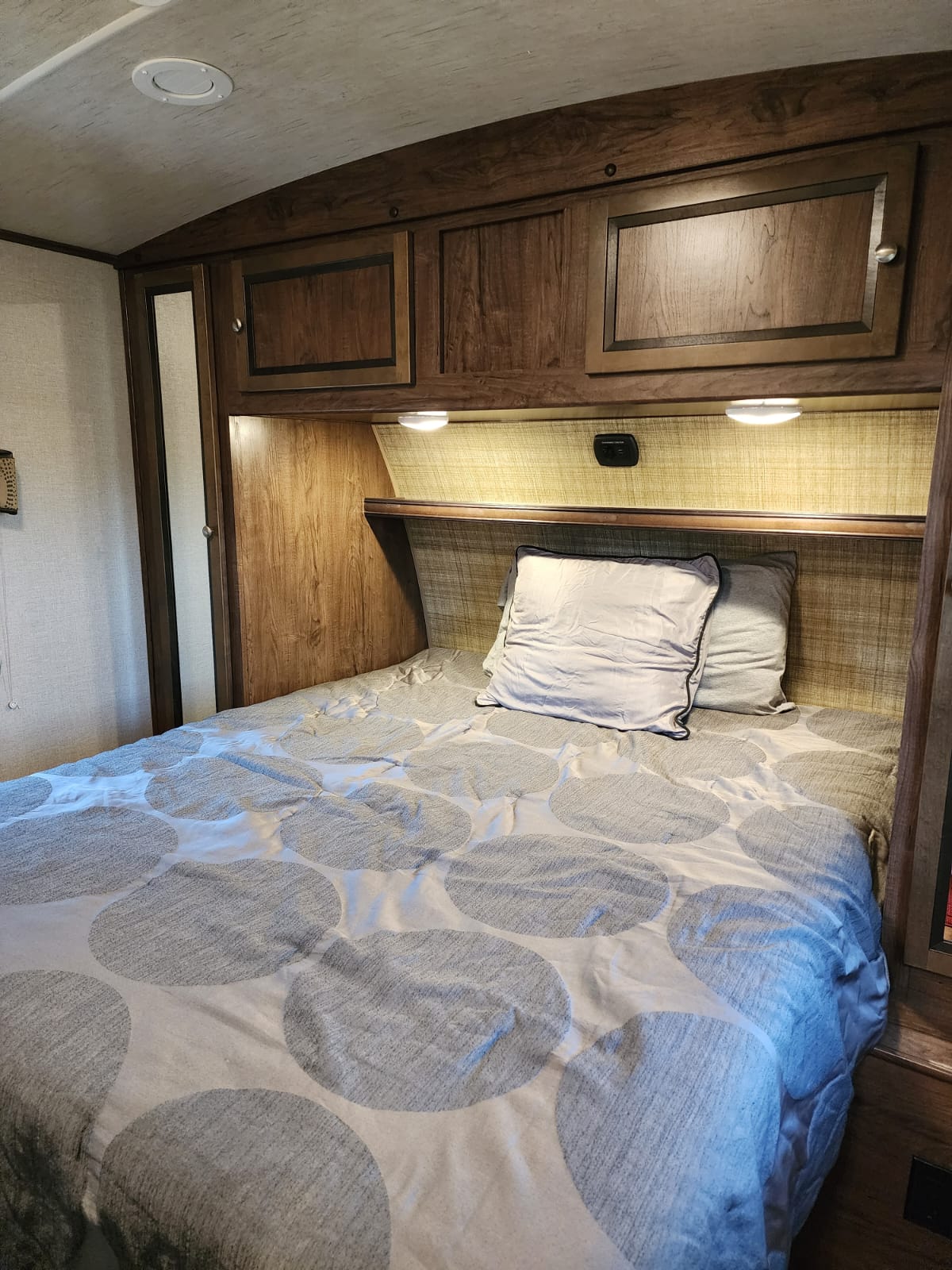 Interior of an RV rental bedroom showing a bed, wood storage cabinets, and LED overhead lights.. Cruiser RV MPG Ultra Lite 2017