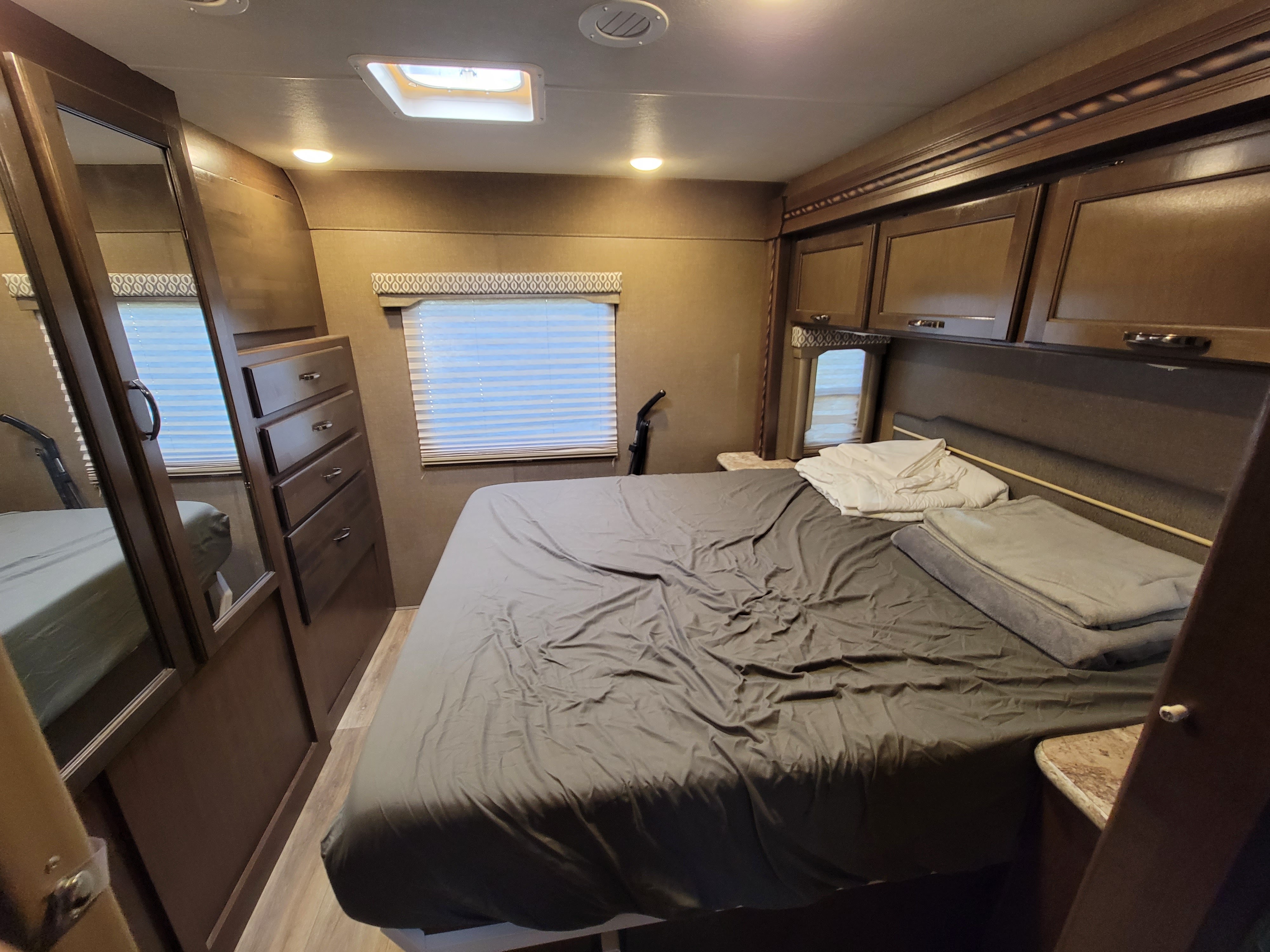 This RV rental's bedroom features a queen bed, mirrored closet, overhead storage, and a window, ideal for comfortable travel.. Thor Freedom Elite 2018