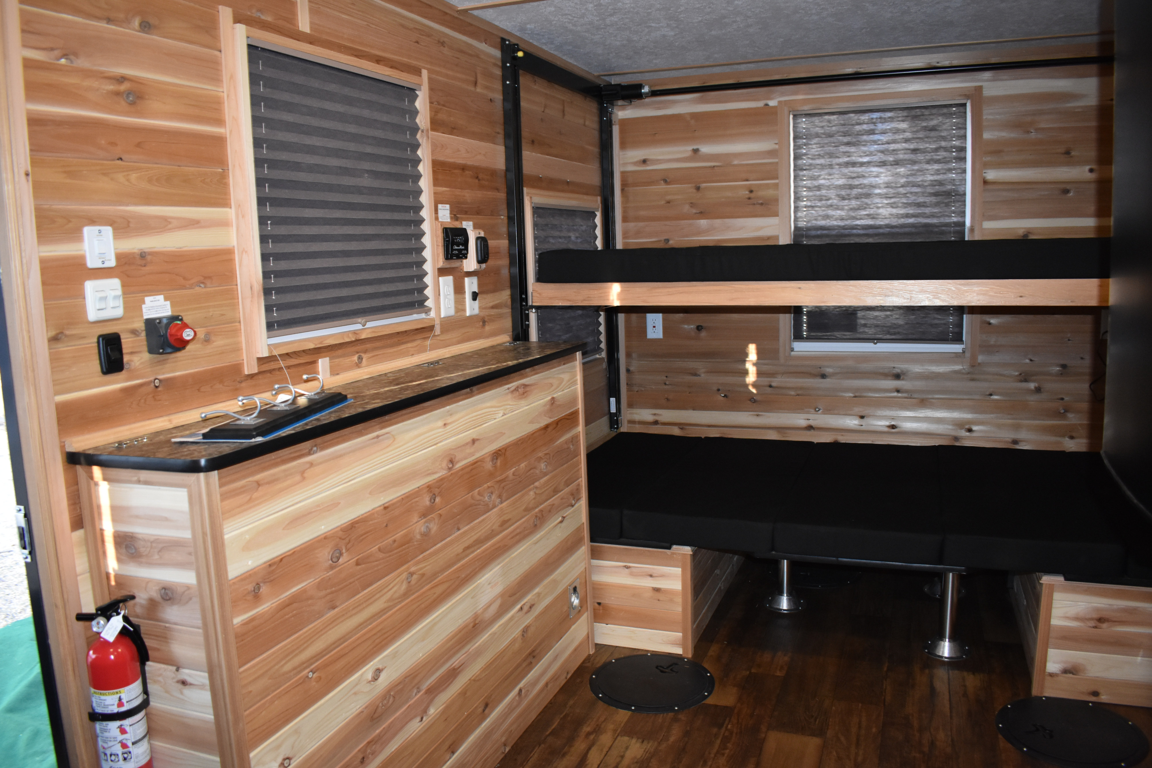 Cozy rv rental interior featuring rustic wood paneling, comfortable bunk beds, and floor openings for ice fishing.. Ice Castle Fish Houses Rv Edition Standard 2024