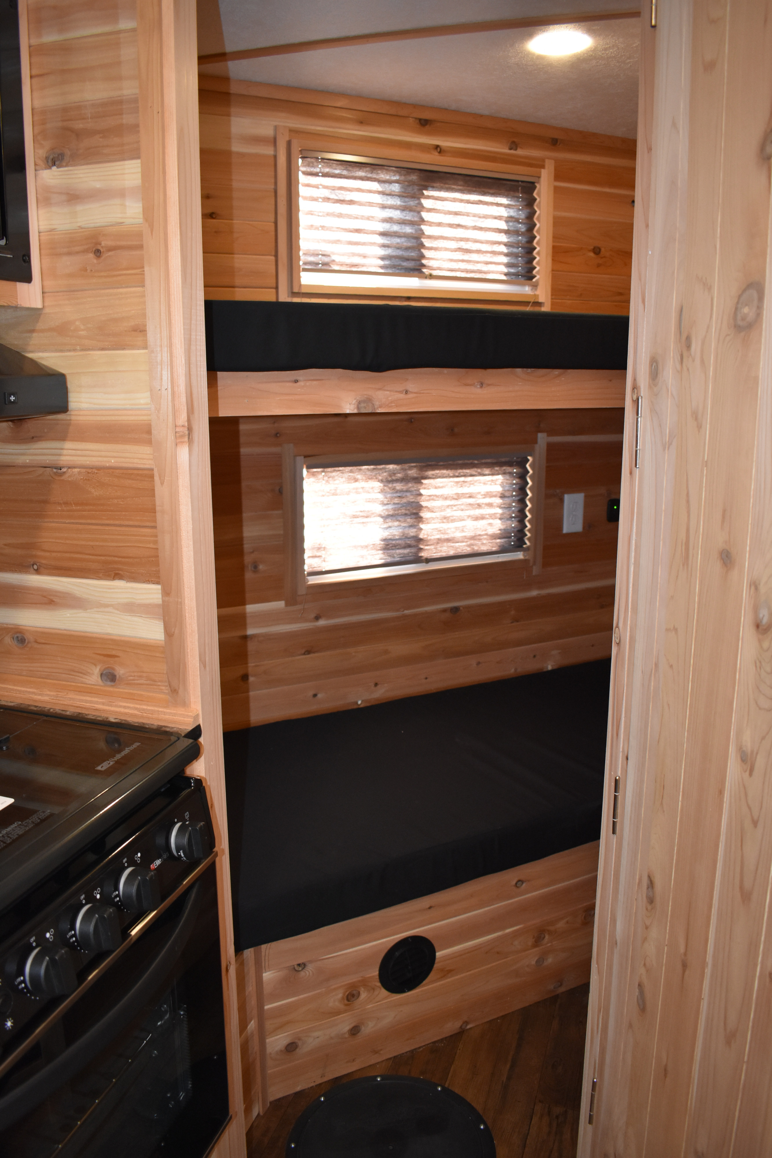 Inside an RV rental: wooden interior with stacked bunk beds, a compact kitchen stove, and windows for cozy adventures.. Ice Castle Fish Houses Rv Edition Standard 2024