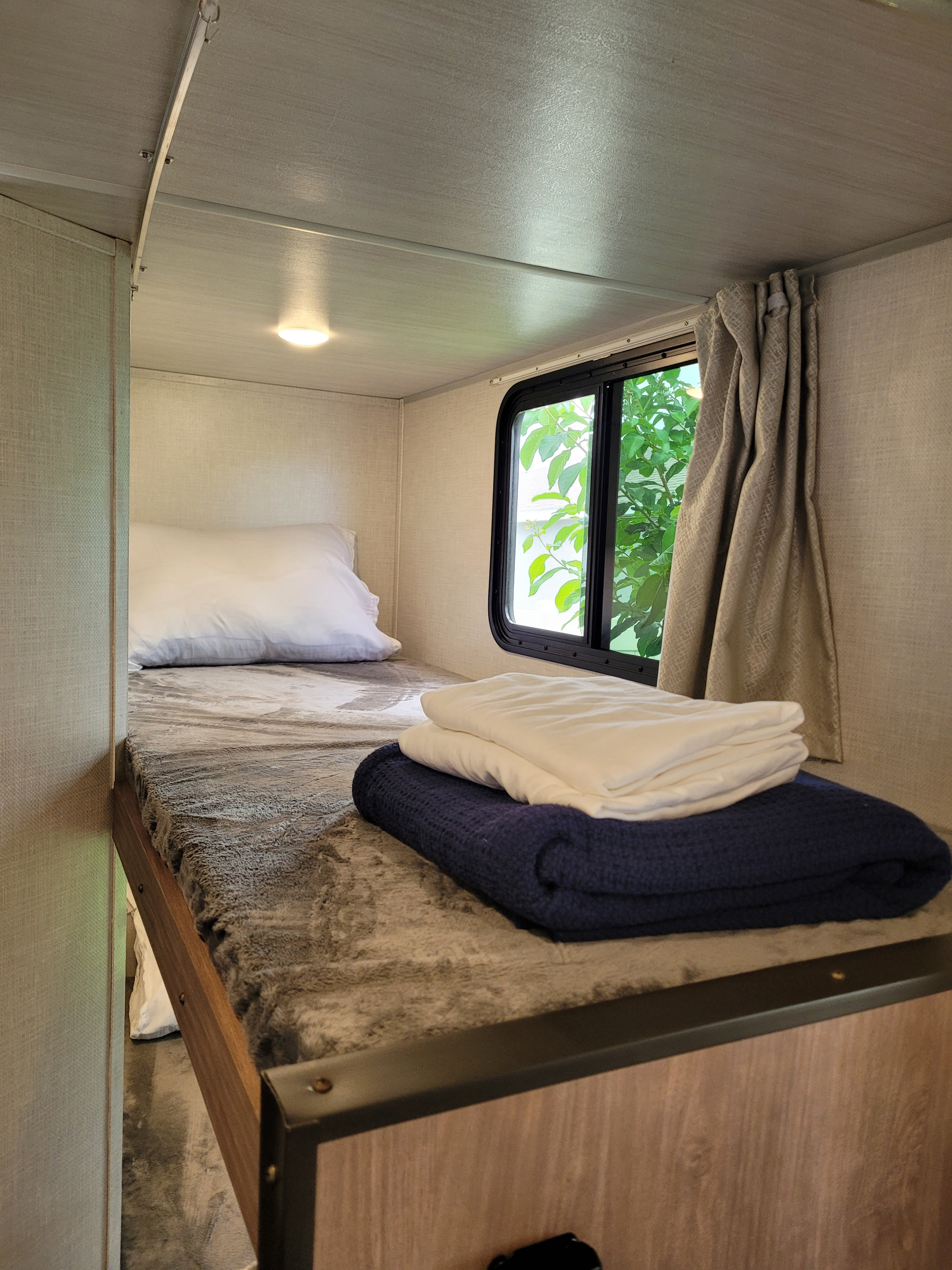 Cozy RV rental bunk bed setup with soft bedding, a window for natural light, and a warm overhead light.. Forest River No Boundaries 2022