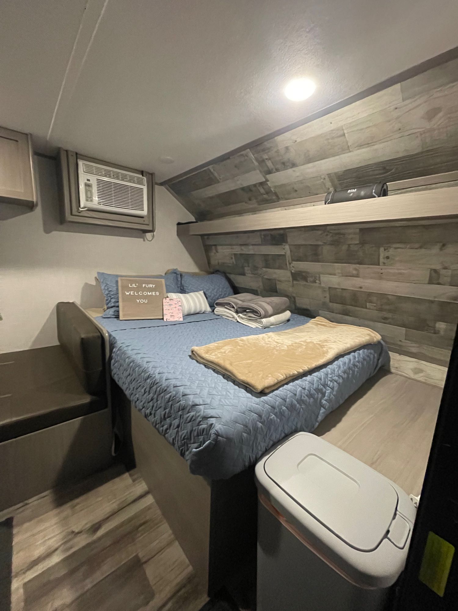 Cozy RV rental bedroom with a comfy bed, air conditioner, wood-paneled walls, and a "Lil' Fury Welcomes You" sign.. Coleman Lantern 17B 2023