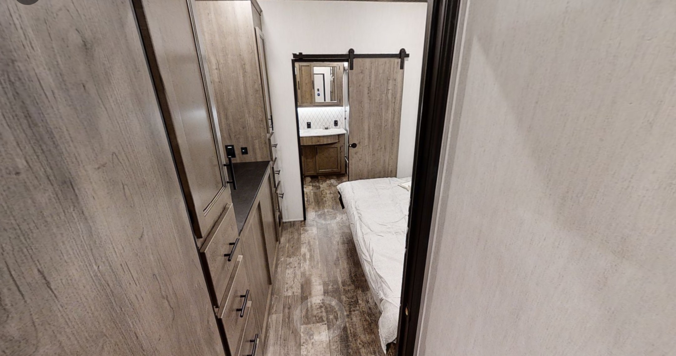Cozy RV rental bedroom and bath. Features a modern interior with wooden cabinets, a bed, and a bathroom with a barn door.. Forest River Sabre 2022