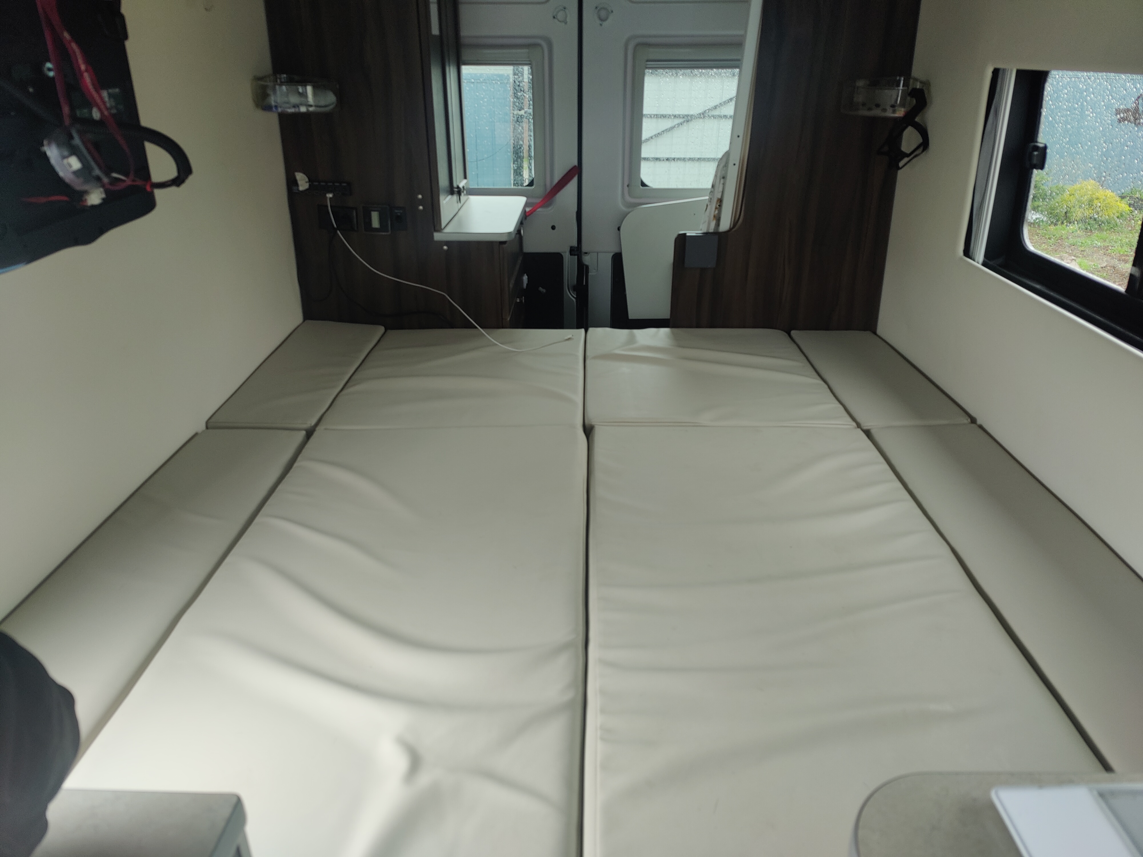 RV rental interior features a modular bed with light cushions, flanked by windows & controls, ready for your travels.. Carado Carado Class B 2018