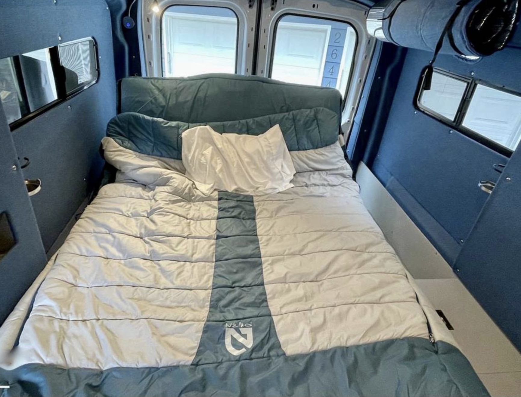 Cozy RV rental interior featuring a large bed with a sleeping bag and pillow. Perfect for comfortable van life adventures.. Ford Transit 2019