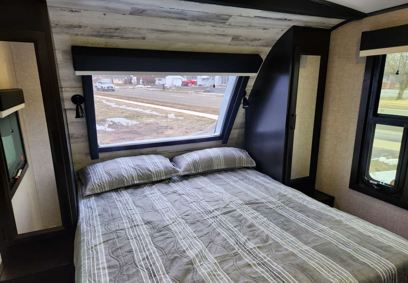 Experience comfort in this RV rental bedroom: cozy bed, panoramic window with street view, and integrated storage.. Jayco Whitehawk 2023