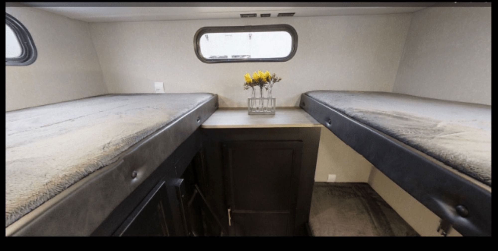 RV rental interior: two cozy bunk beds flank a central table with flowers, beneath an oval window.. Forest River Cherokee Grey Wolf 2022
