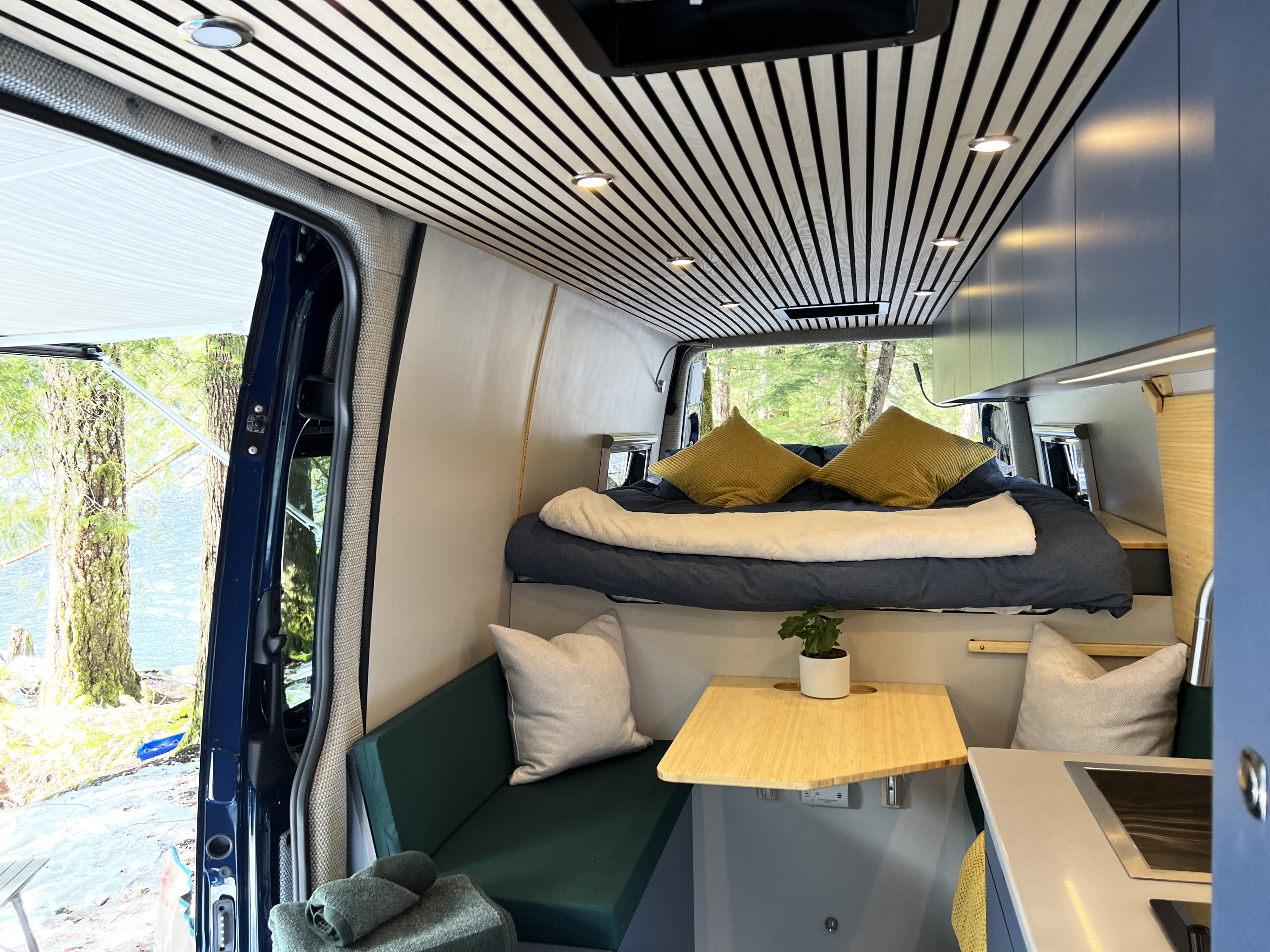 Explore in comfort! This rv rental camper van interior boasts a cozy bed, kitchenette, seating, and scenic lakeside view.. Mercedes Sprinter 2022