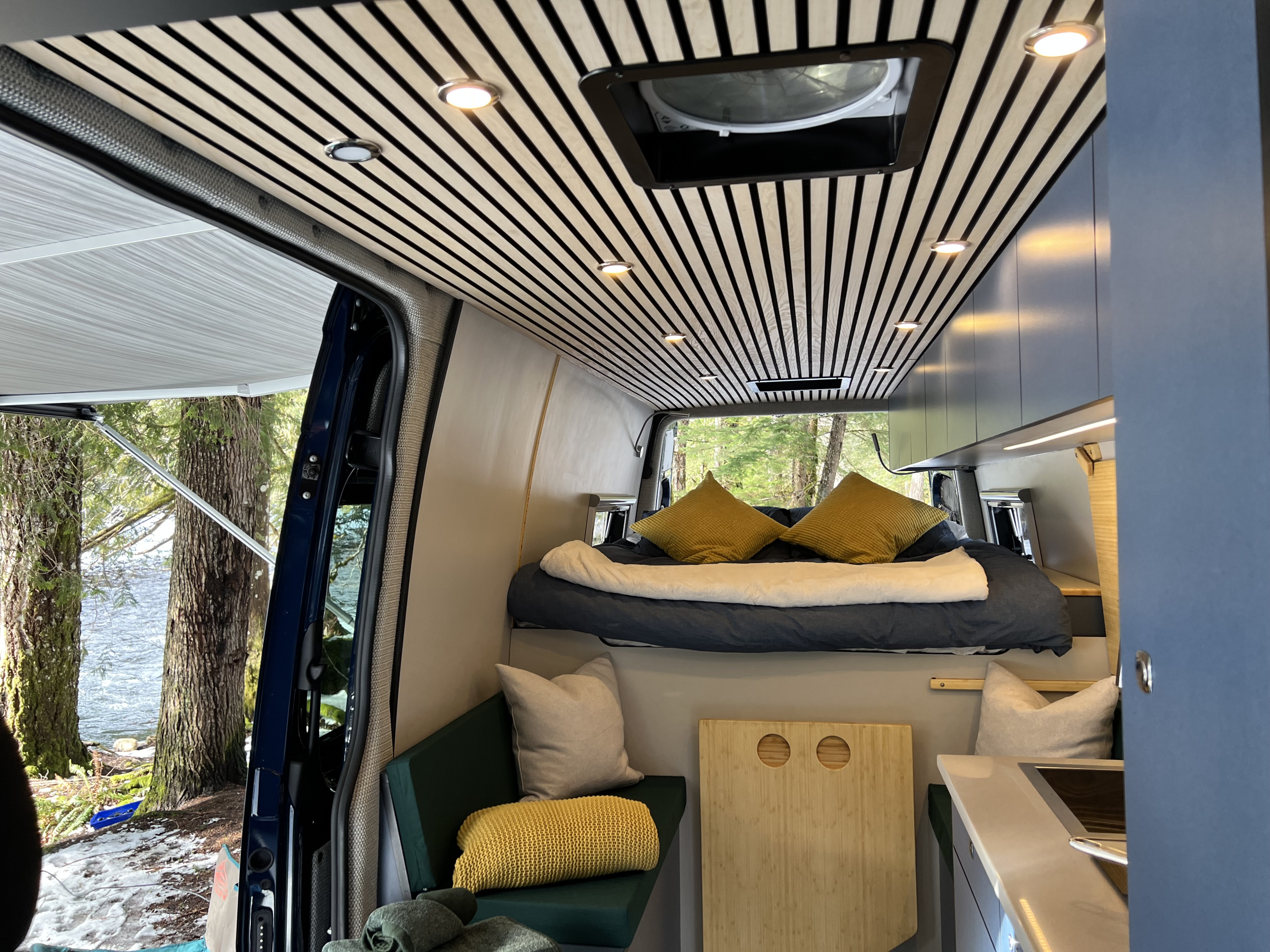 RV rental: Cozy camper van interior with slatted wood ceiling, comfy bed, seating area, and a beautiful outdoor river view.. Mercedes Sprinter 2022