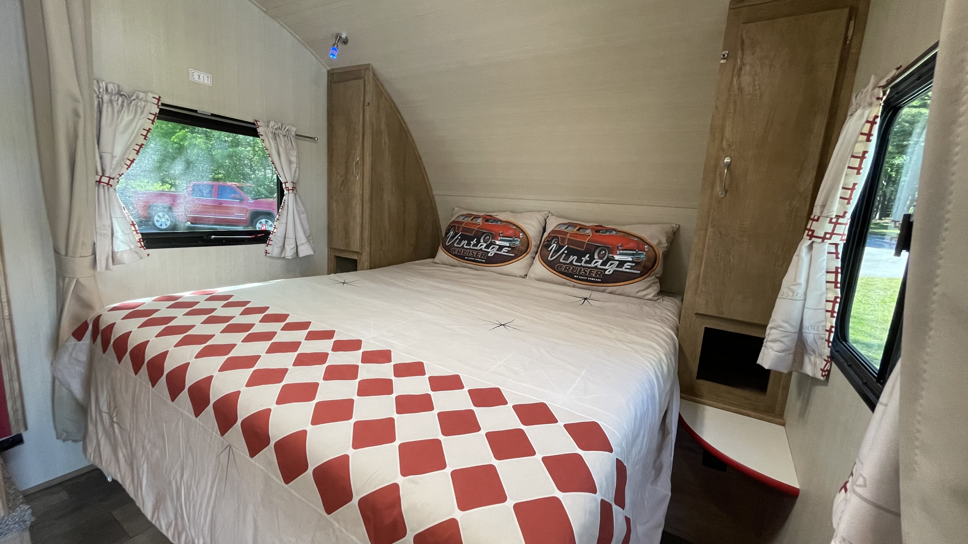 Cozy RV rental bedroom featuring a checkered bedspread, "Vintage Cruiser" pillows, and a view of a red truck outside.. Gulf Stream Vintage Cruiser 2021