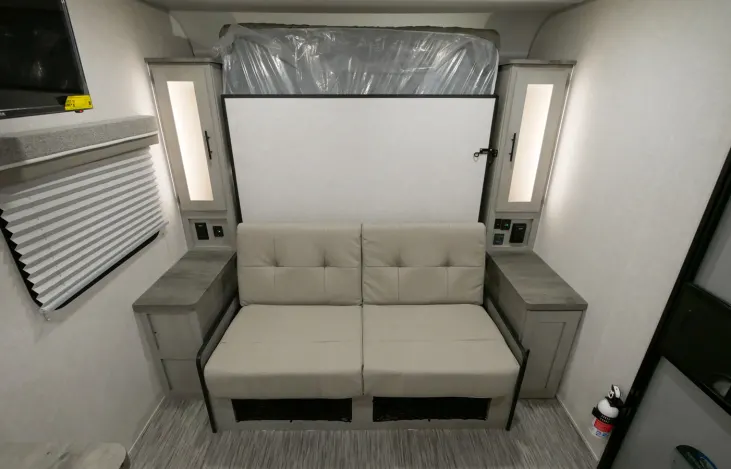 RV rental interior: a beige sofa below a folded Murphy bed, with side cabinets and a TV for compact, comfortable living.. Forest River IBEX 19MBH 2022