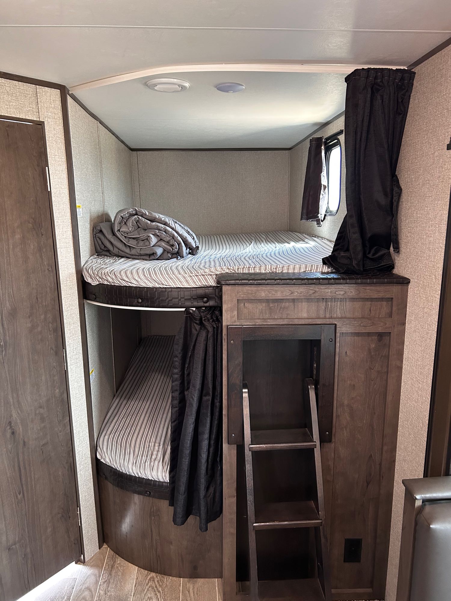 RV rental interior with two bunk beds (striped mattresses, curtains) and a wooden ladder for access. Compact sleeping space.. Jayco Jay Flight SLX 2021