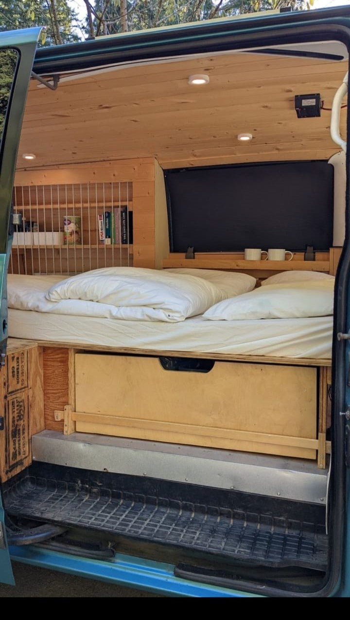 RV rental: A cozy, wooden-paneled camper van interior featuring a comfy bed, pull-out storage, and a built-in bookshelf.. Chevrolet Other 1996