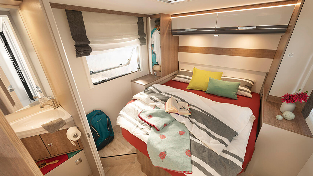 Comfortable RV rental interior: a compact bedroom with bed, storage, window, and a functional sink area for travel.. Dethleffs TREND 90 T 7057 DBM 2023