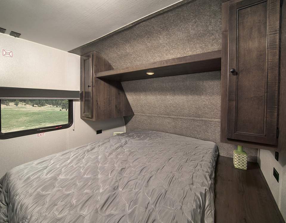 Cozy RV rental bedroom with a gray bed, wood cabinets, and window overlooking a field, ideal for travel.. Starcraft Autumn Ridge 2021