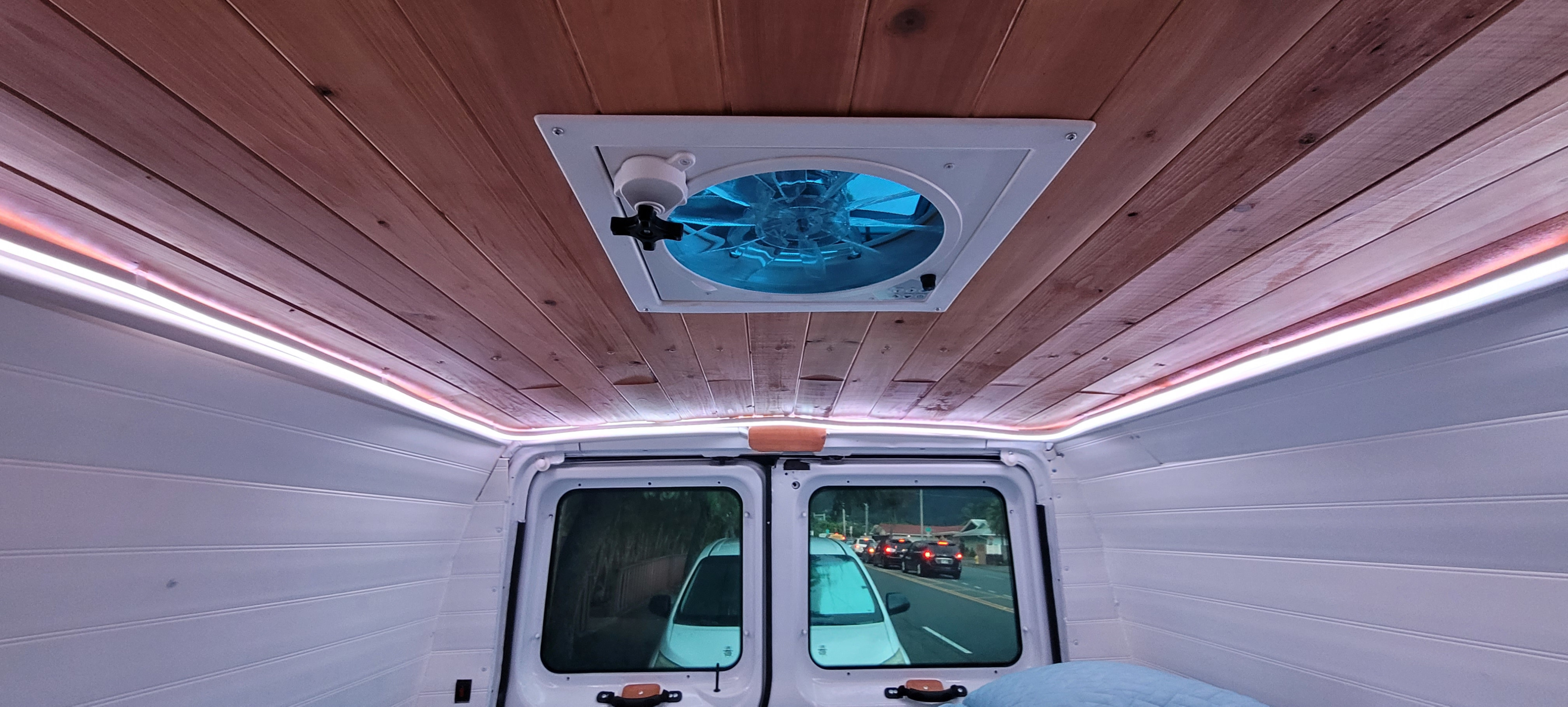 Inside a customized RV rental: wood plank ceiling, bright blue fan, ambient LED lighting, and a view of traffic through rear windows.. Ford E250 2009