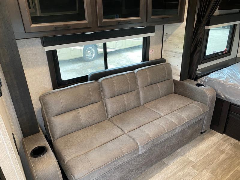 RV rental interior: spacious light brown sofa with built-in cup holders, large windows, and overhead cabinets. A cozy living space.. Jayco 166 FBS 2022