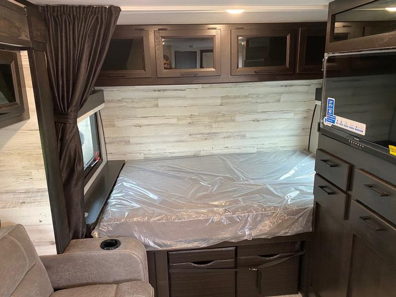 RV rental interior: Clean bedroom area with plastic-covered bed, wall-mounted TV, and dark wood storage cabinets.. Jayco 166 FBS 2022