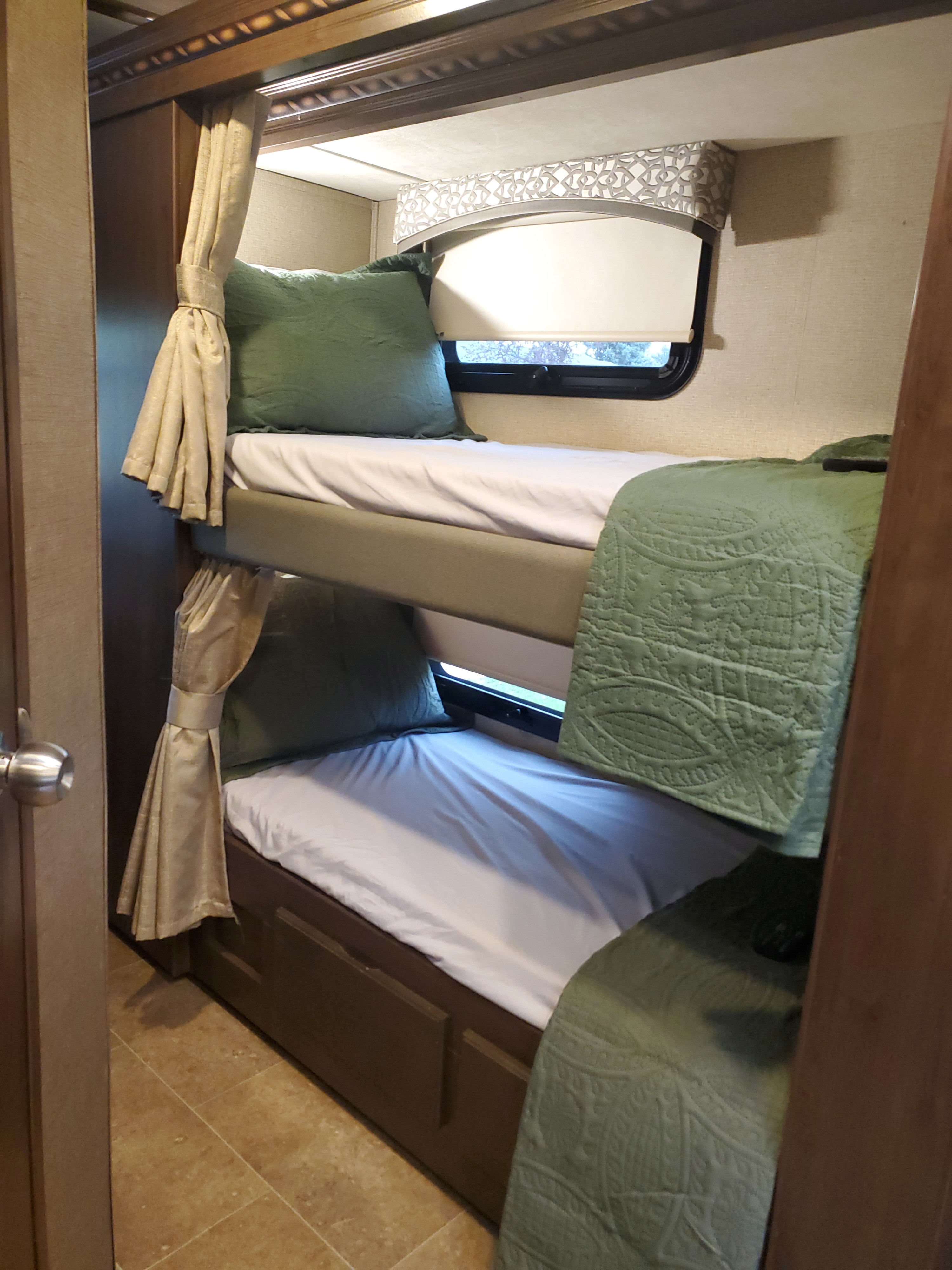 Inside an RV rental: two bunk beds with crisp white sheets, green pillows & quilts, and small windows with shades.. Thor Chateau 2018