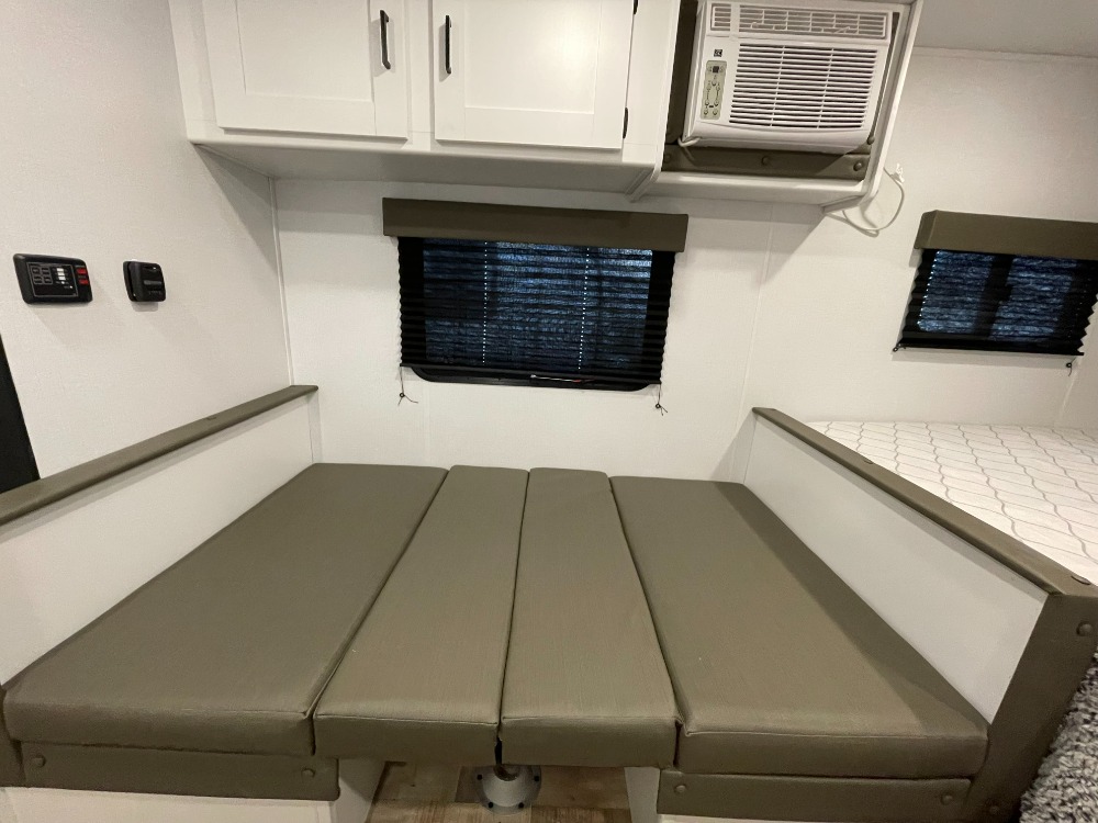 This RV rental interior shows a dinette seating area transformed into a bed, featuring an overhead AC, wall controls, and windows.. Keystone RV Hideout 2022